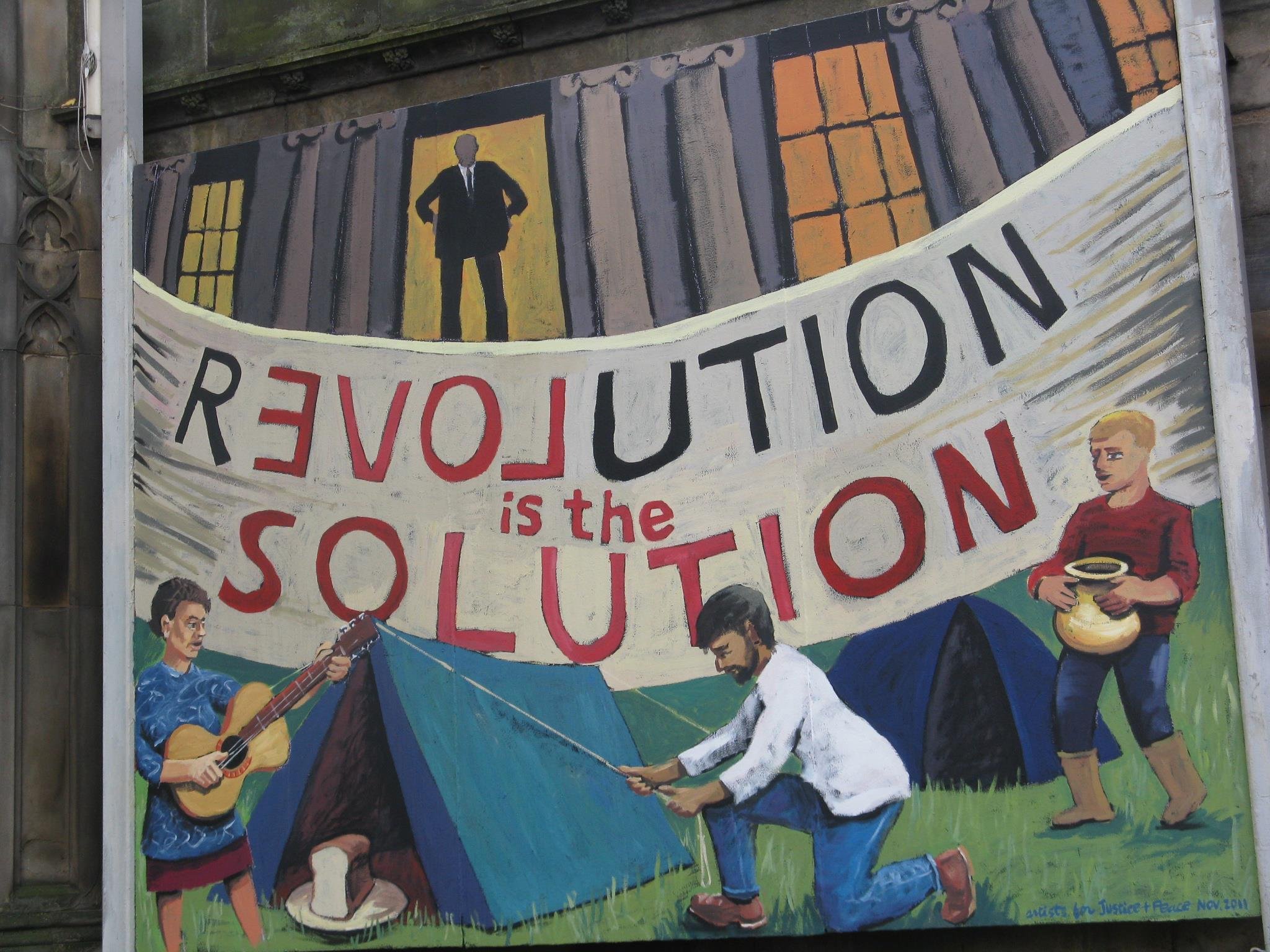 A mural painted on a wall depicts a protest scene with people holding a large banner. The banner contains the word 'REVOLUTION' in large letters, with some words partially obscured. The scene includes characters, one playing a guitar and others holdi