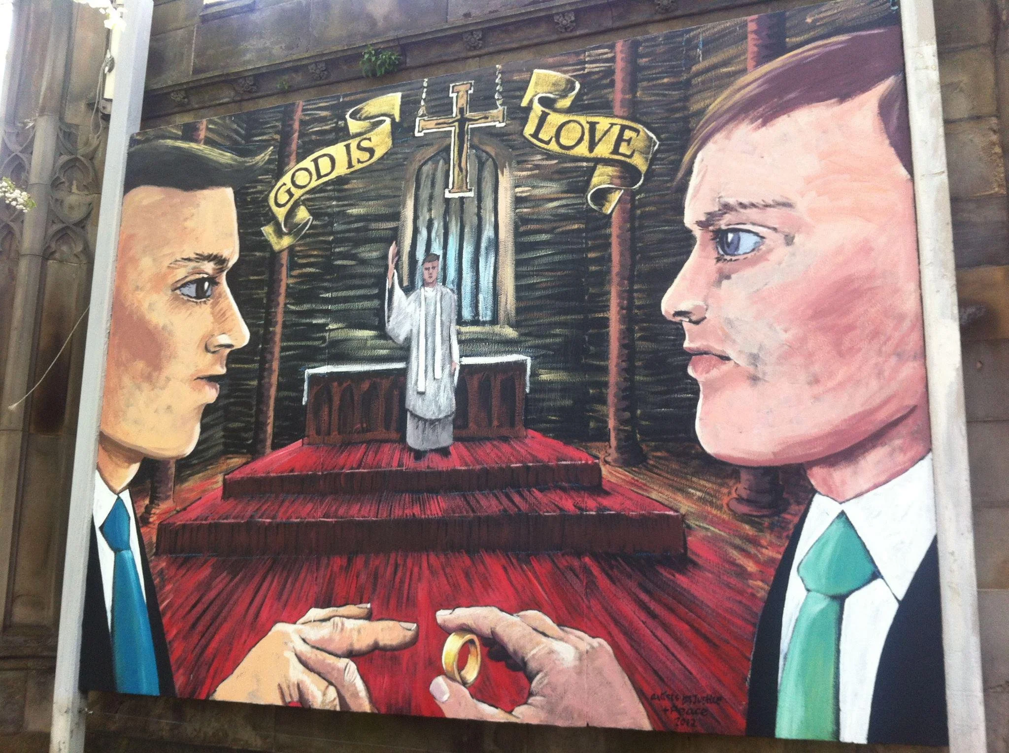 A painting depicting two women facing each other, with a church-like interior scene in the background. The woman on the left has dark hair and a blue tie, while the woman on the right has reddish-brown hair and a green jacket. Above them, a banner re