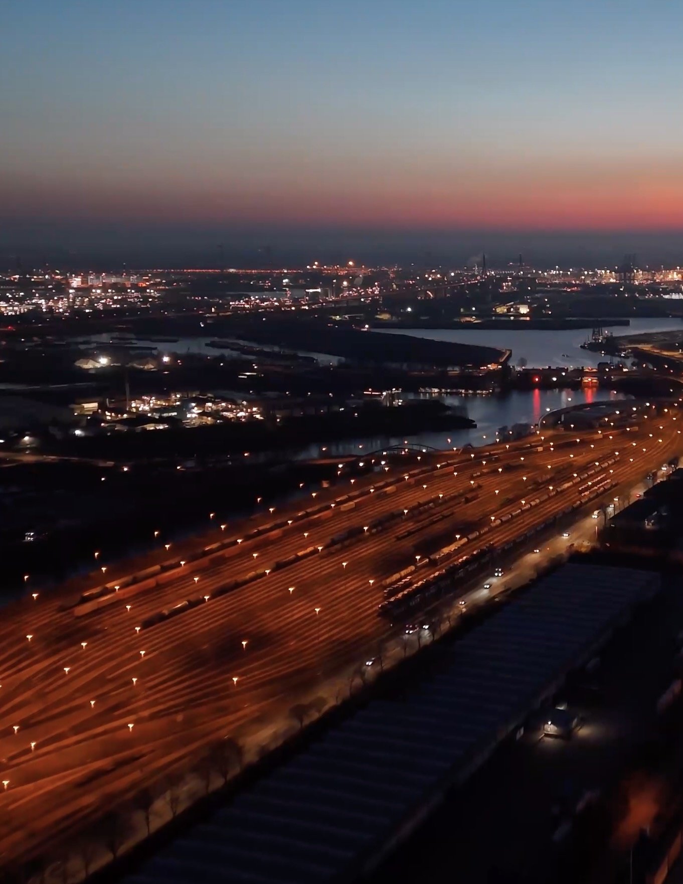 Aerial view of a highway next to a shipping yard with numerous stacked shipping containers.