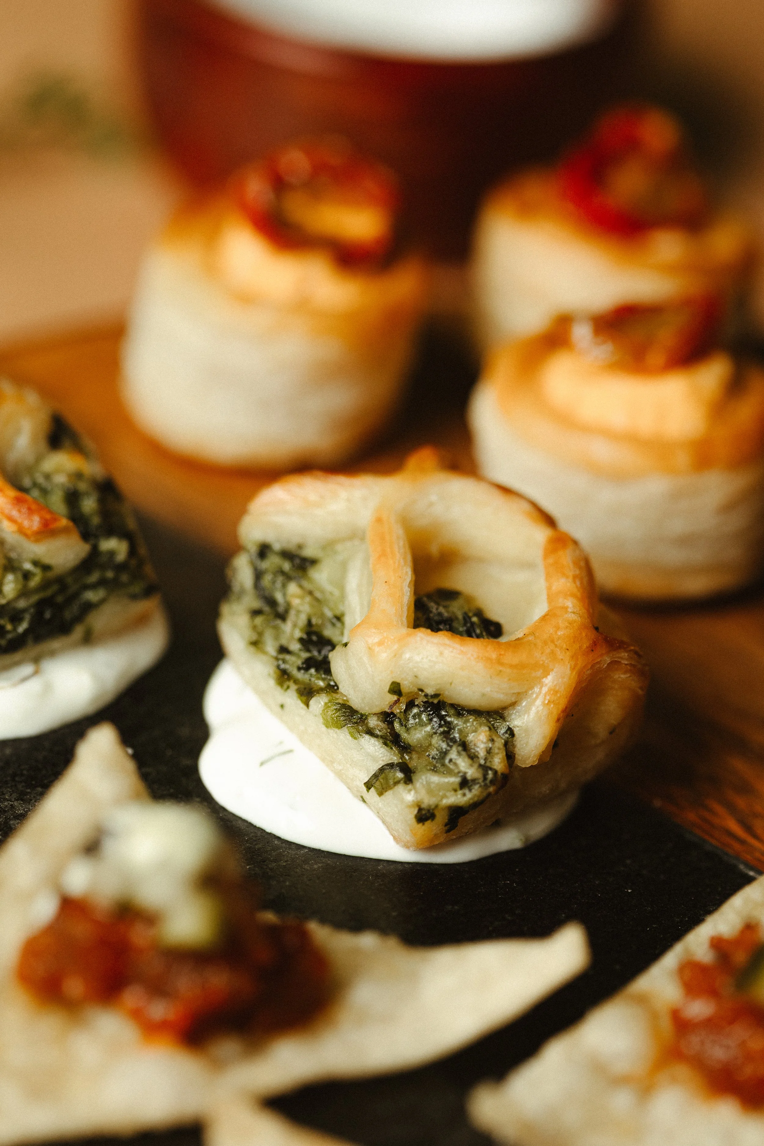 Close-up of assorted small appetizers on a black serving tray, including vegetable or herb-filled pastry bites.