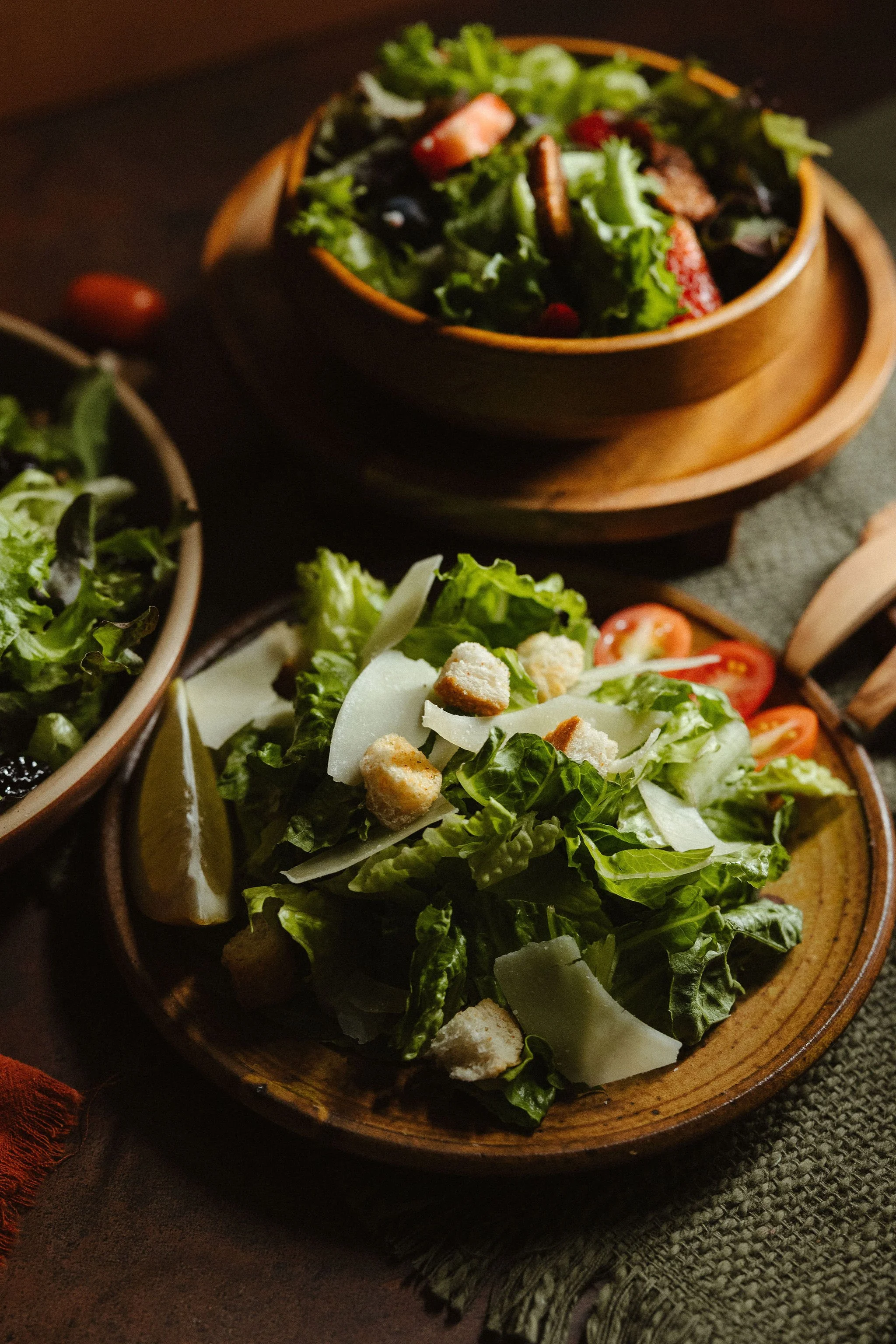 Various salads in wooden bowls on a dark table. The focus is on a fresh green salad with croutons, cheese, cherry tomatoes, and lettuce.