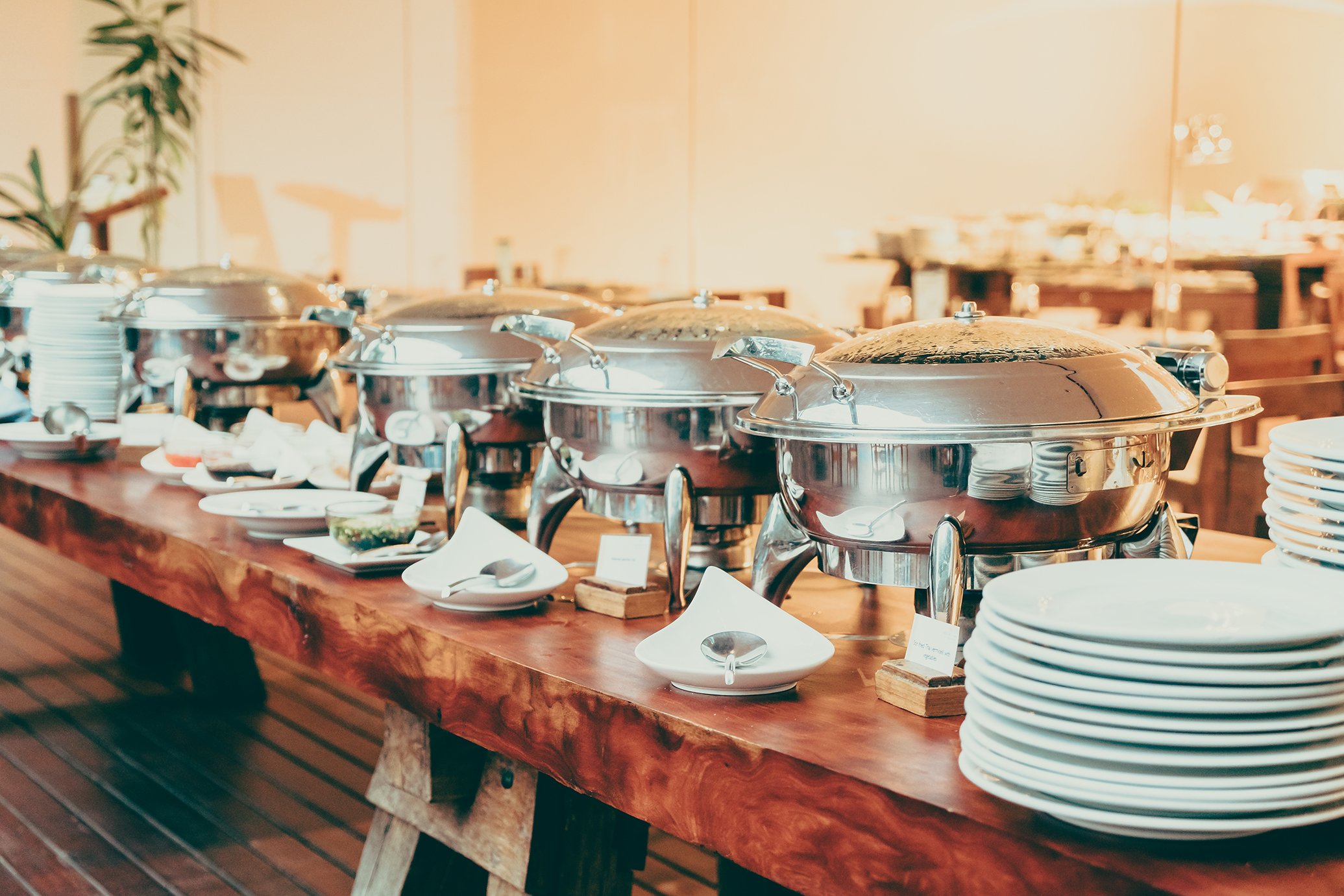 Buffet table with chafing dishes, plates, and condiments at a restaurant buffet.