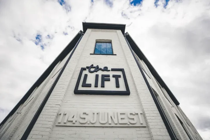Low-angle view of a white brick building with a sign that reads 'the LIFT' and an address '114 S JUNE ST' on the front.