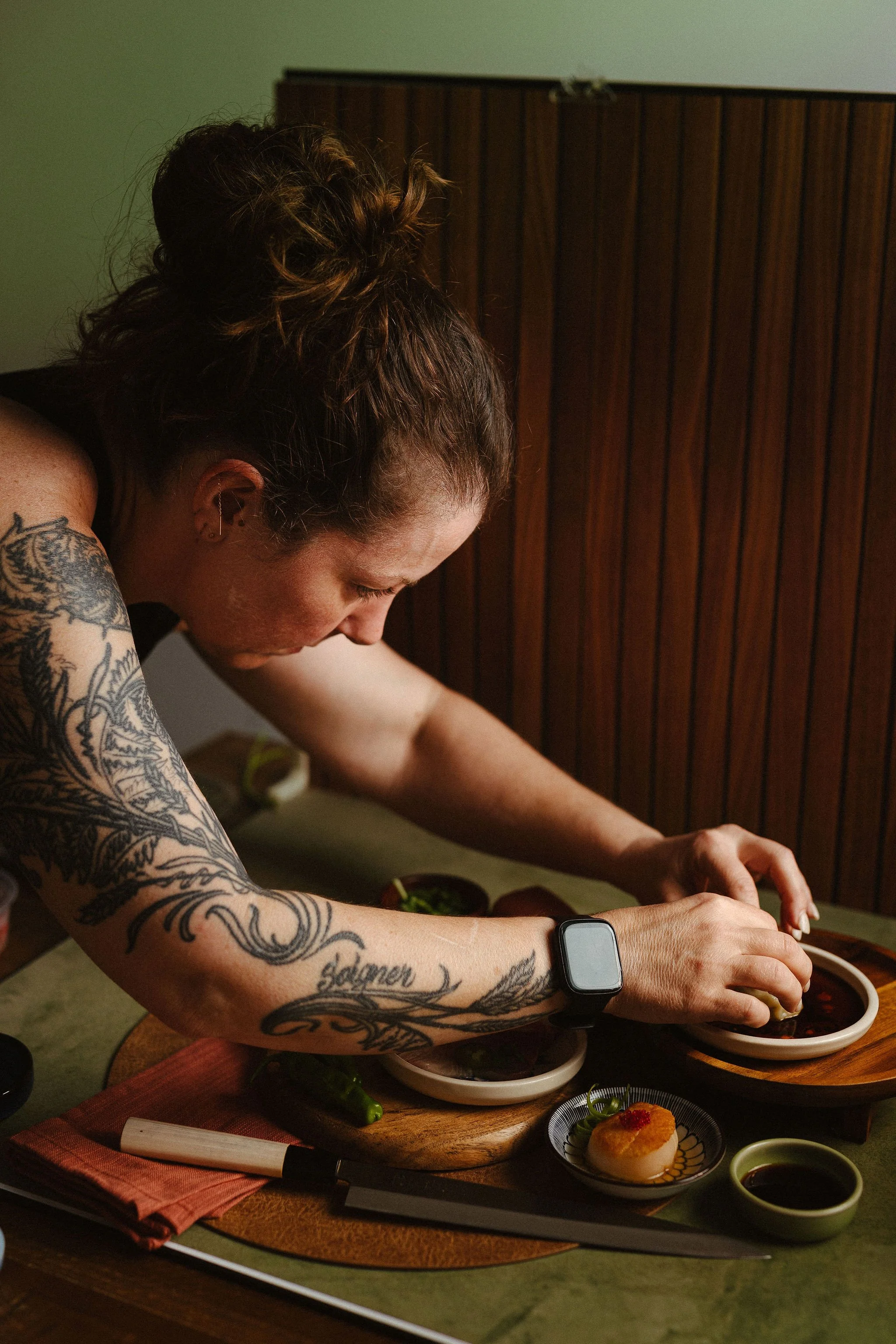 A woman preparing sushi at a wooden table in a dimly lit room.