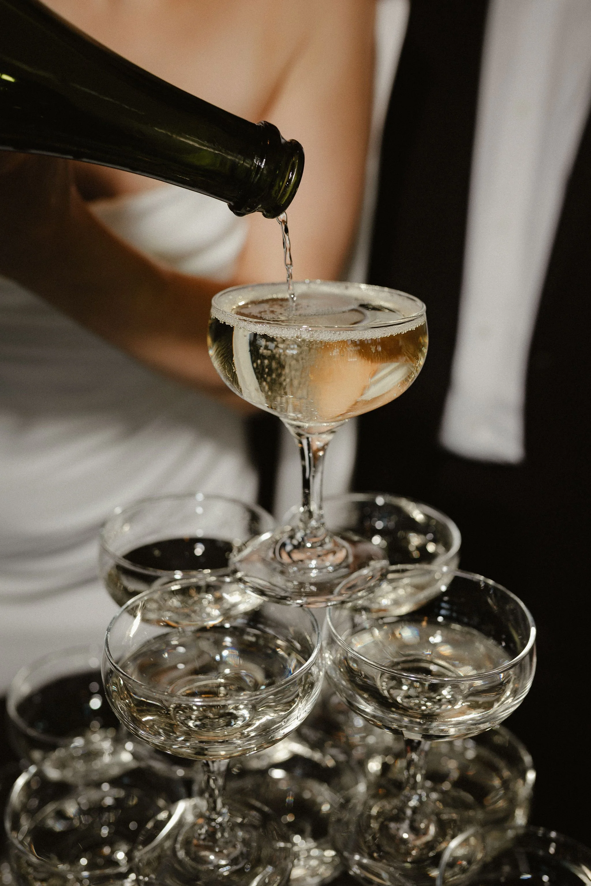 A person is pouring champagne into a glass in a tower of stacked glasses for a celebration.