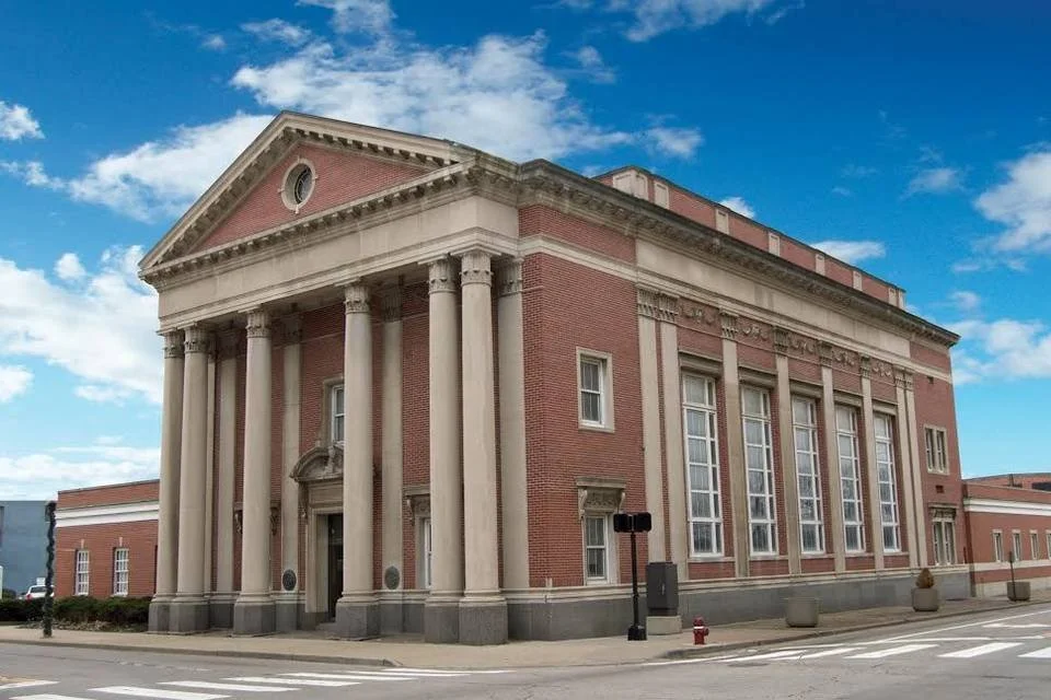 Front view of a historic red brick building with large columns and multiple windows under a partly cloudy sky.