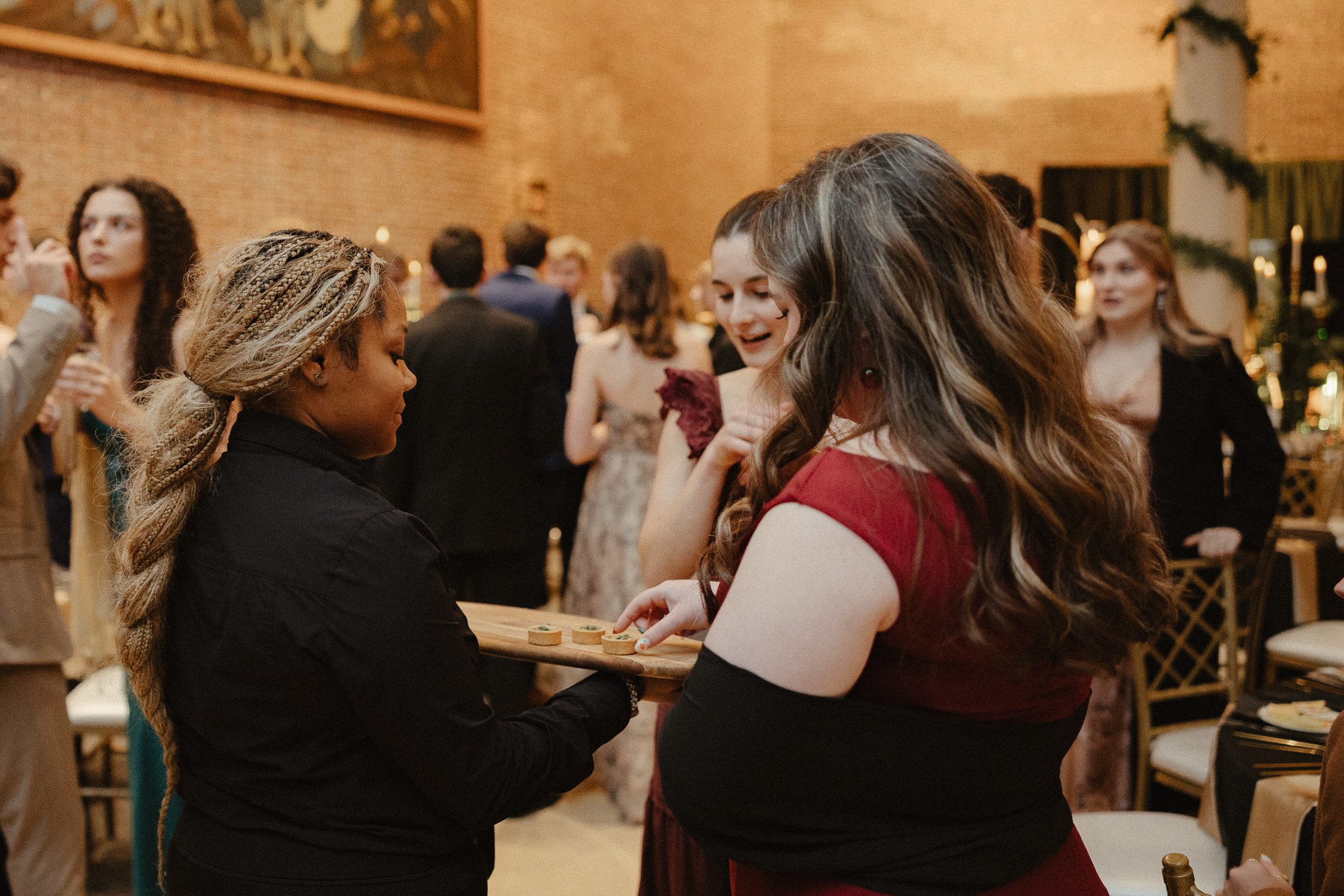 People at a social gathering, engaging in conversation and sharing a drink, with warm lighting and festive decorations in the background.