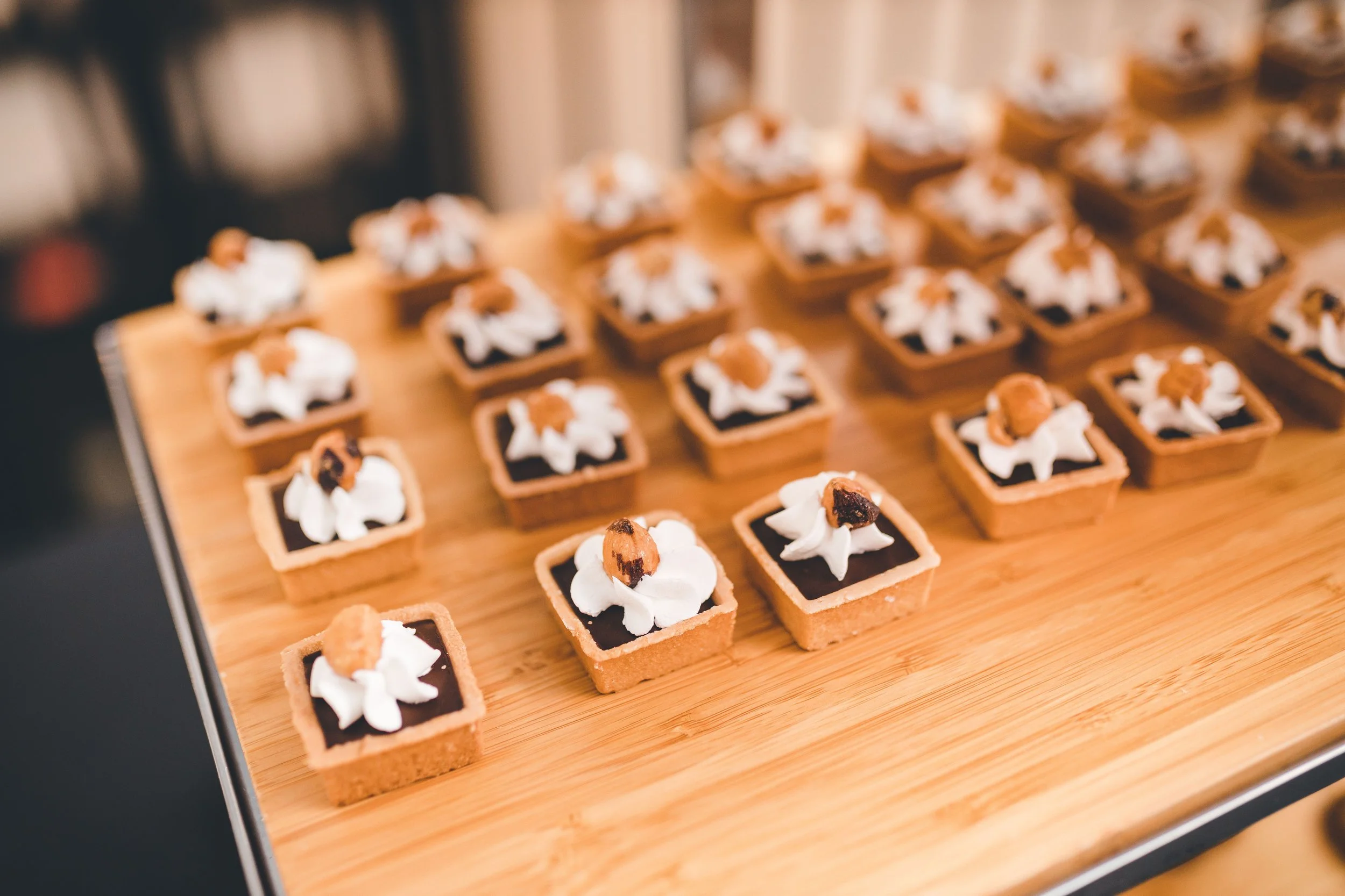 A tray of small square desserts with a chocolate layer topped with whipped cream and a small piece of caramel or toffee.