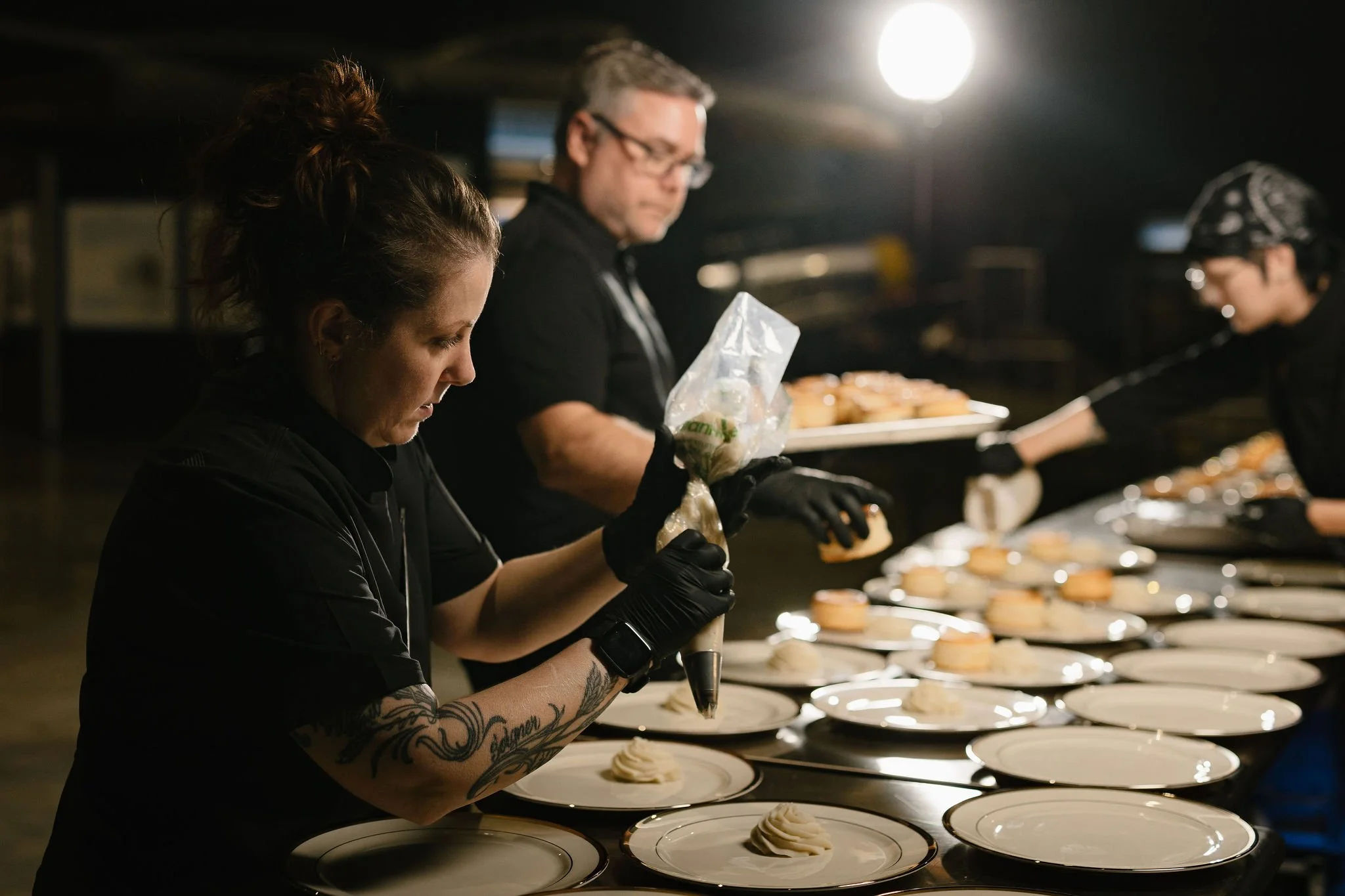 People working in a professional kitchen, decorating cakes on a conveyor belt in a bakery or cake shop.