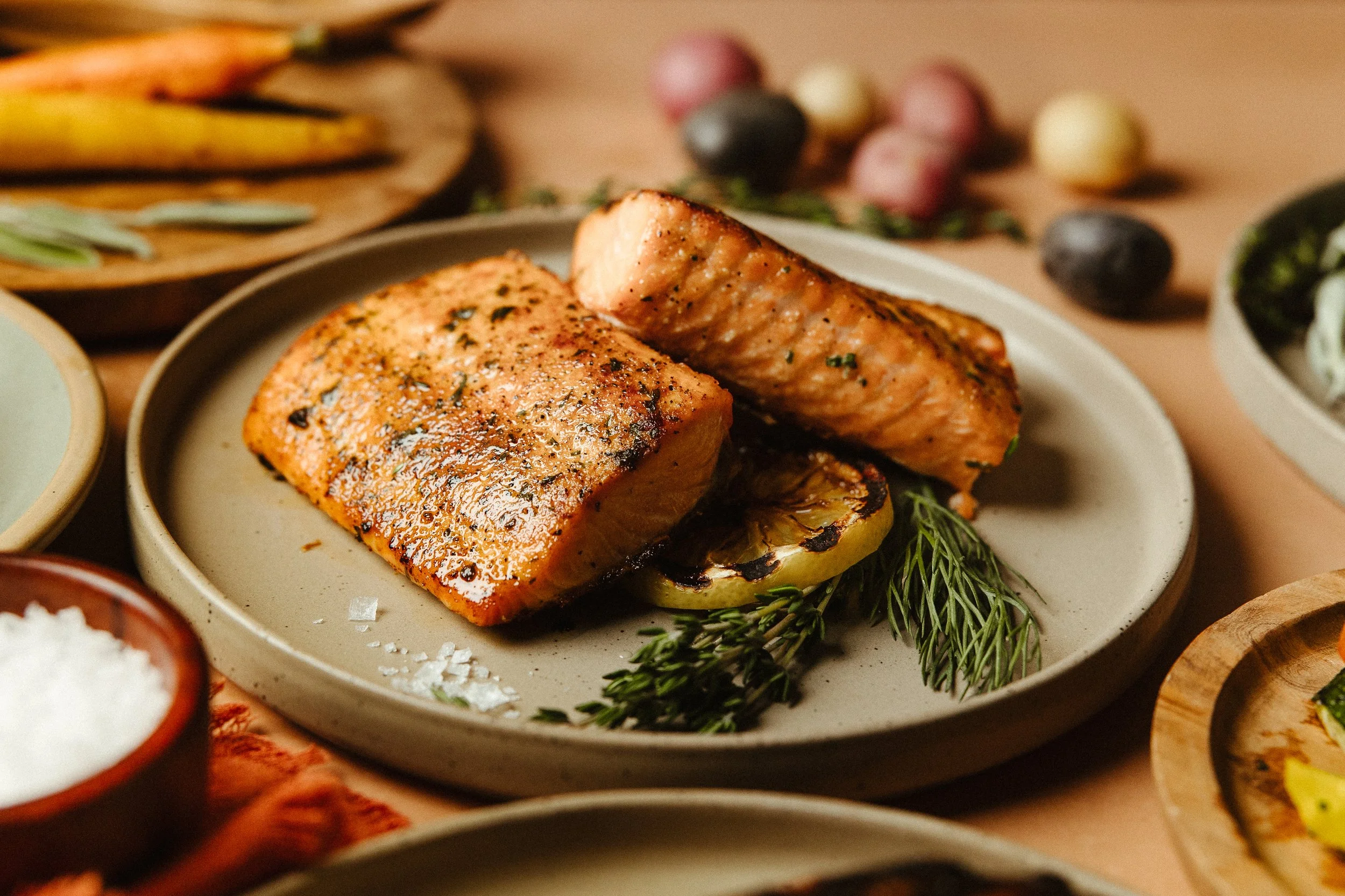 Grilled salmon fillet on a plate with herbs, surrounded by various side dishes and vegetables.
