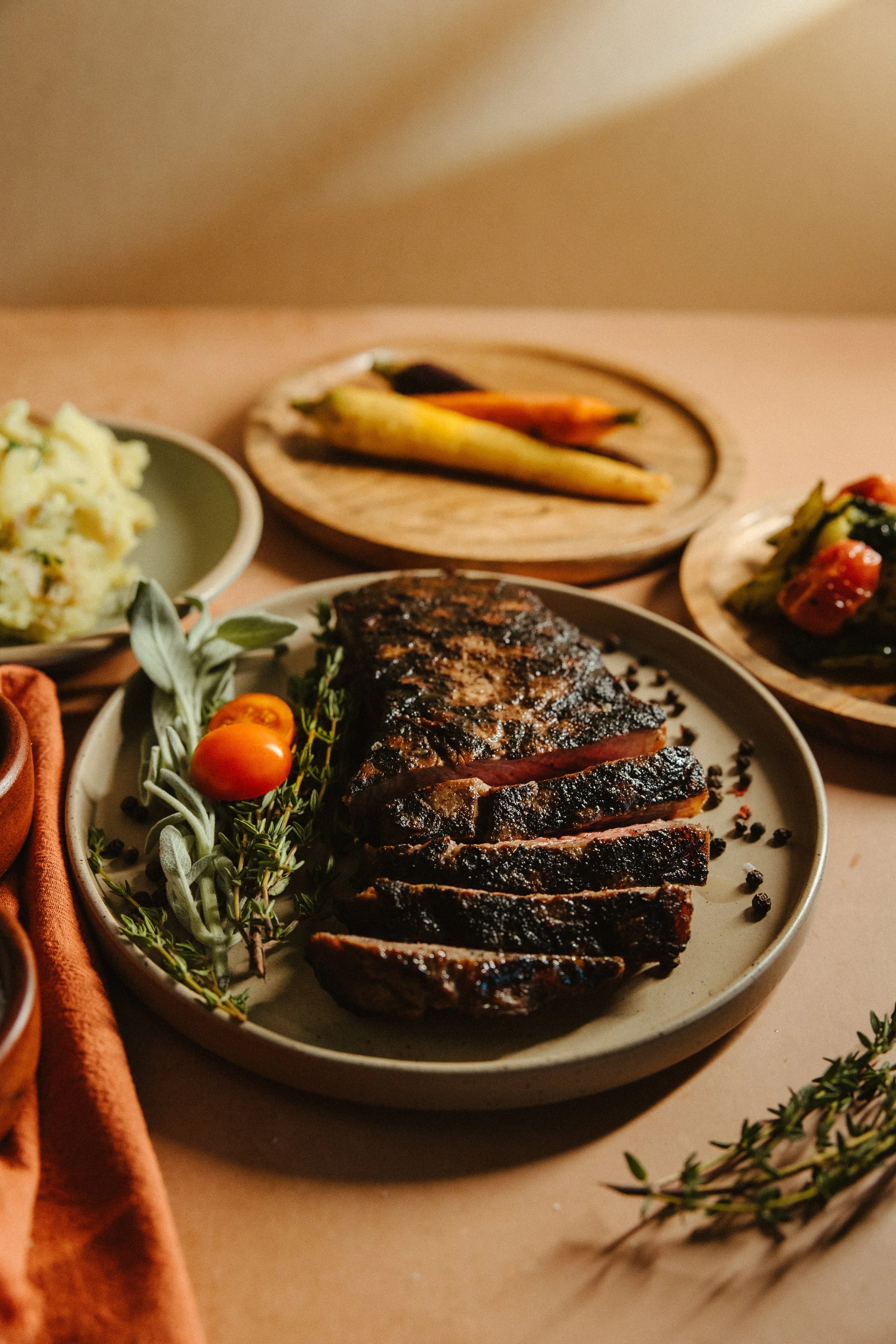 Slices of grilled beef steak with black pepper, garnished with fresh rosemary and cherry tomatoes on a ceramic plate.