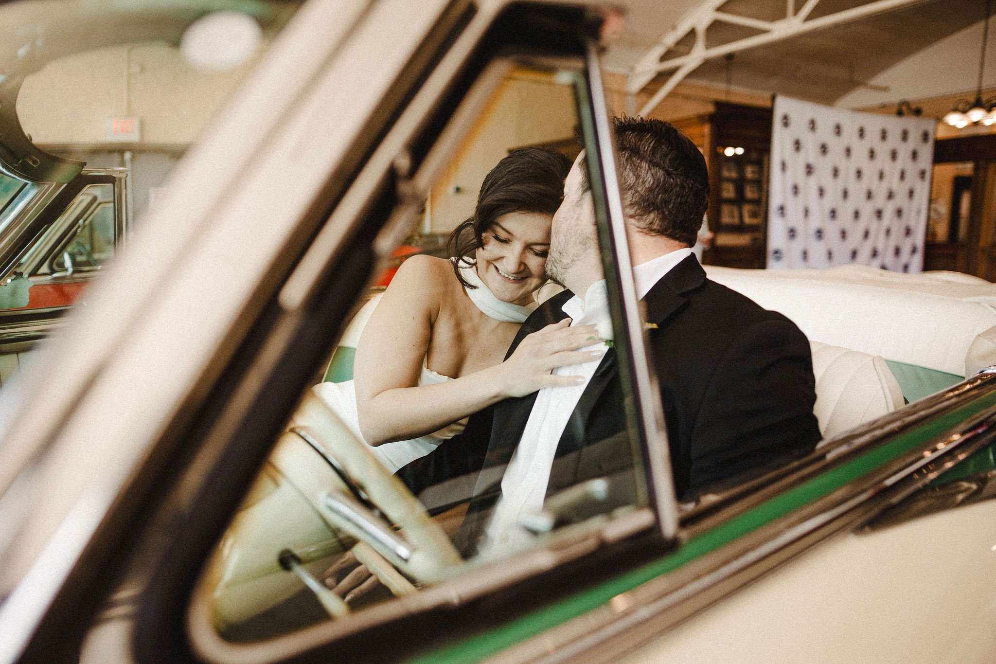 A couple sharing an intimate moment, smiling and leaning close to each other inside a vintage car.