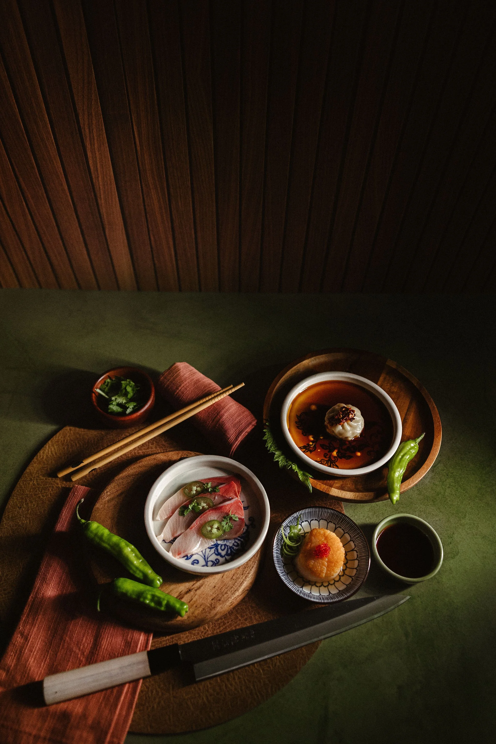 A Japanese meal with various dishes including sashimi, tofu, and green peppers, arranged on a wooden tray with chopsticks.
