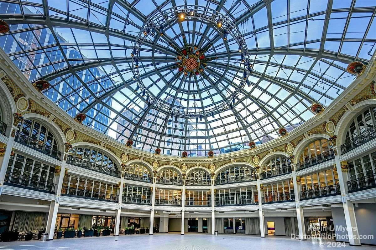 Interior view of a grand atrium with a large glass-domed ceiling, ornate balconies, and a decorative chandelier hanging at the center of the ceiling.