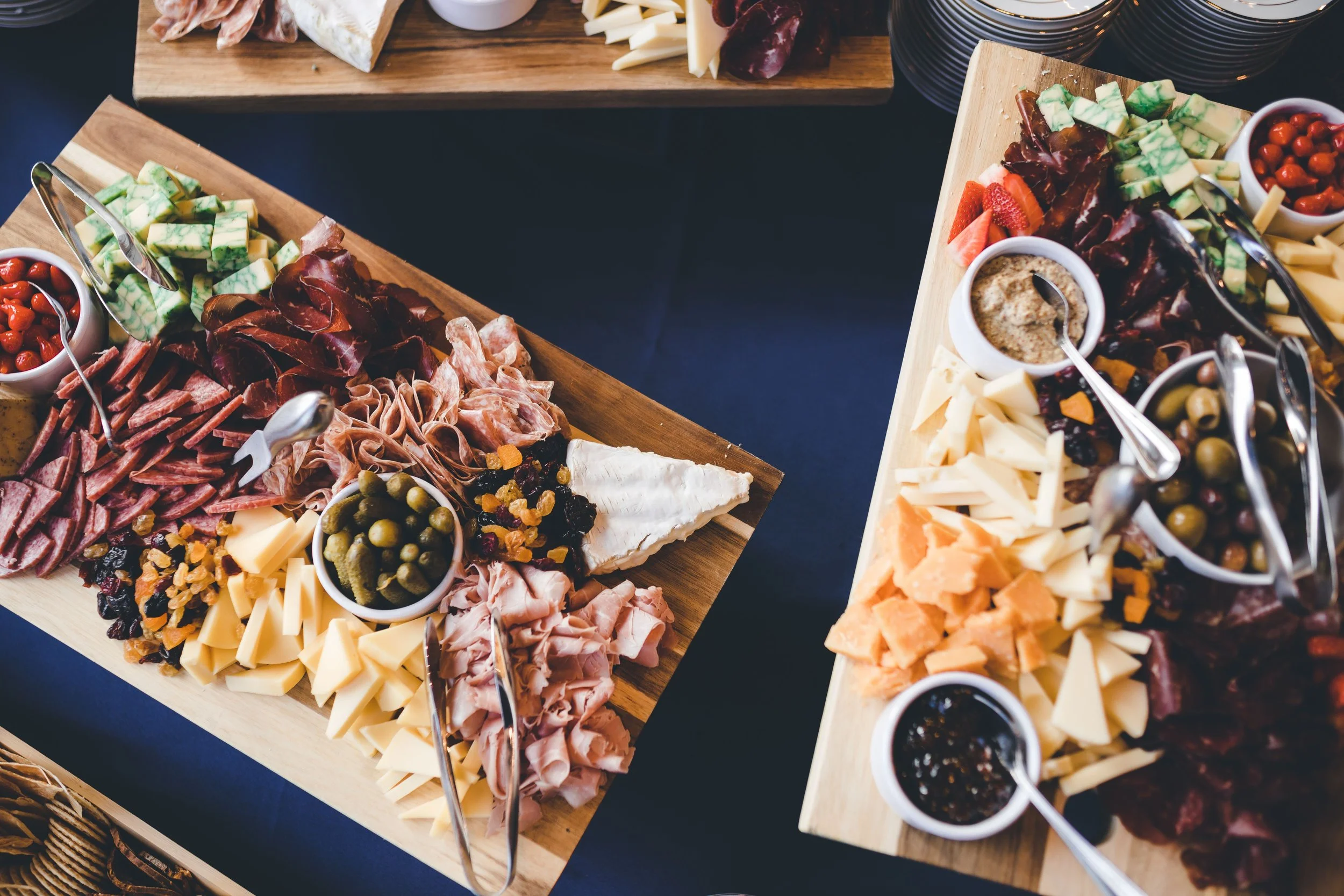 A cheese and charcuterie board with assorted cheeses, meats, fruits, nuts, dried fruits, olives, and dipping sauces on wooden boards.