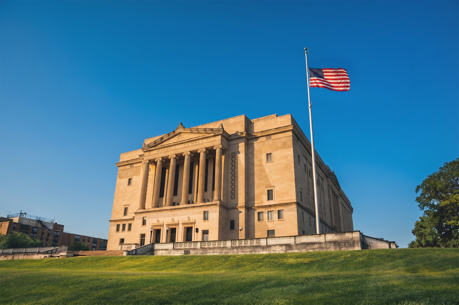 The United States Masonic Temple building with a flagpole and American flag in front, under a clear blue sky, with green grass in the foreground.