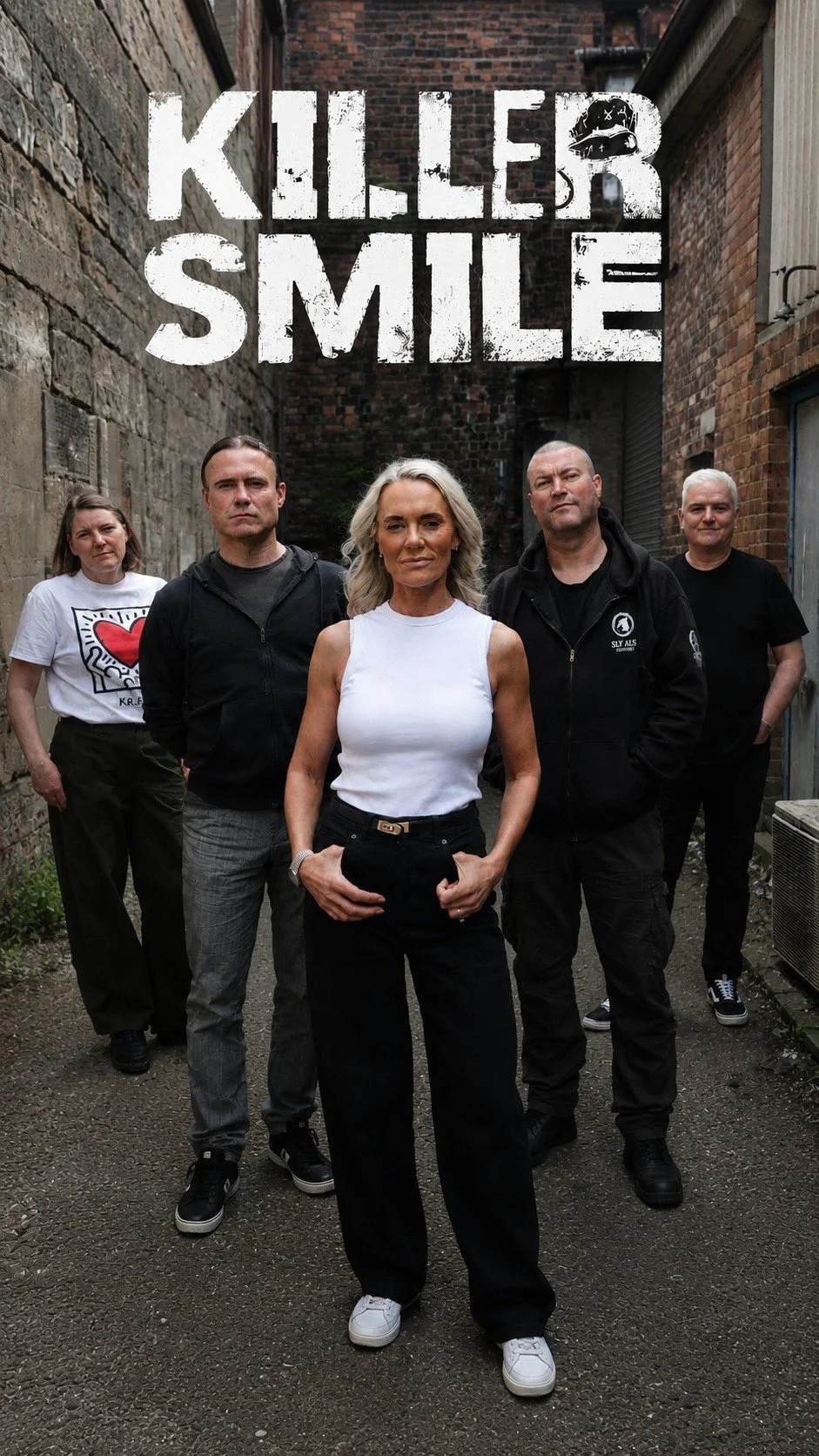 A group of five people standing in a narrow alley with brick walls, with text overlay 'Killer Smile' at the top, featuring three women and two men, all dressed casually.