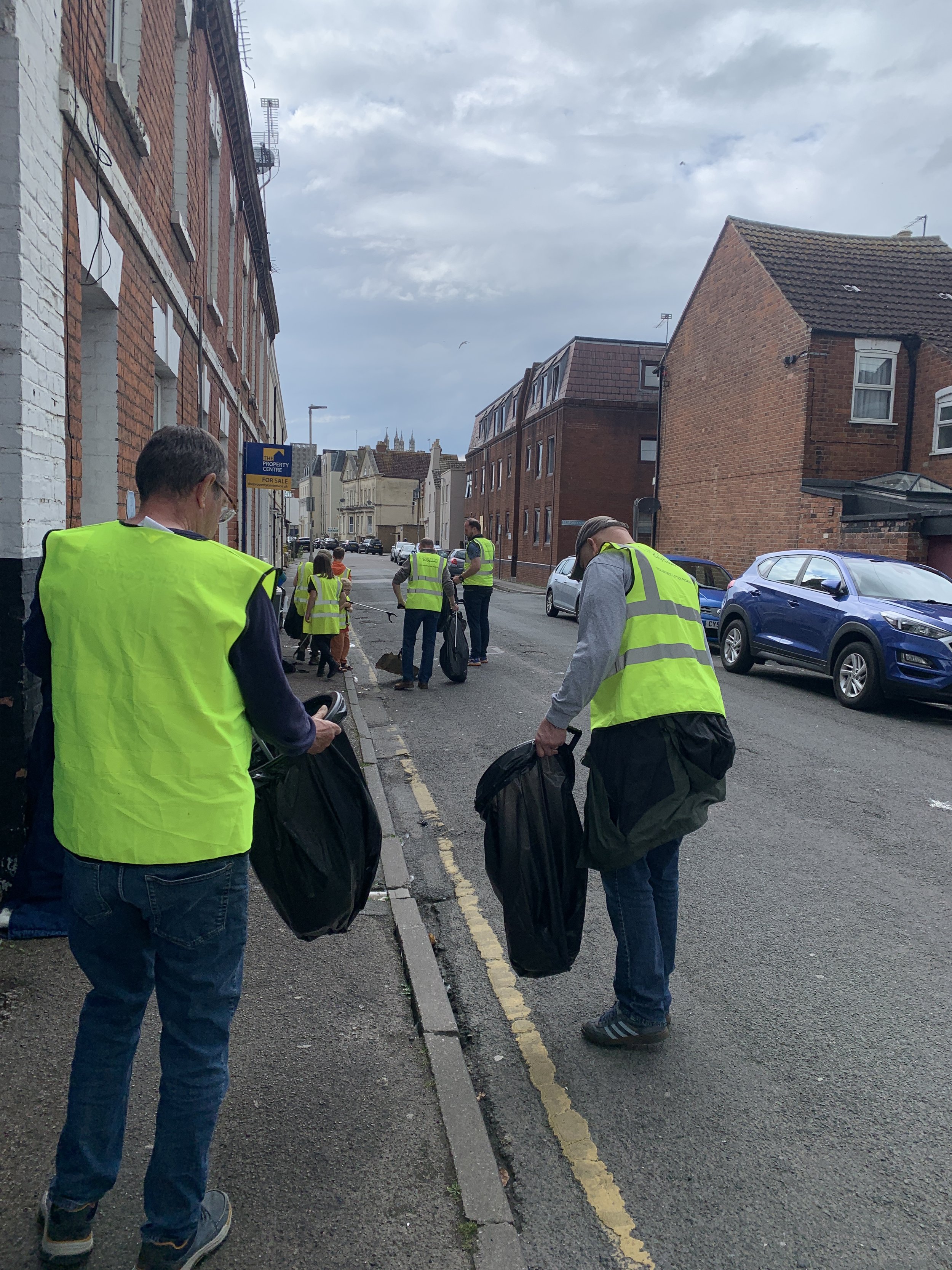 Group of people wearing yellow safety vests cleaning up trash on a city street.