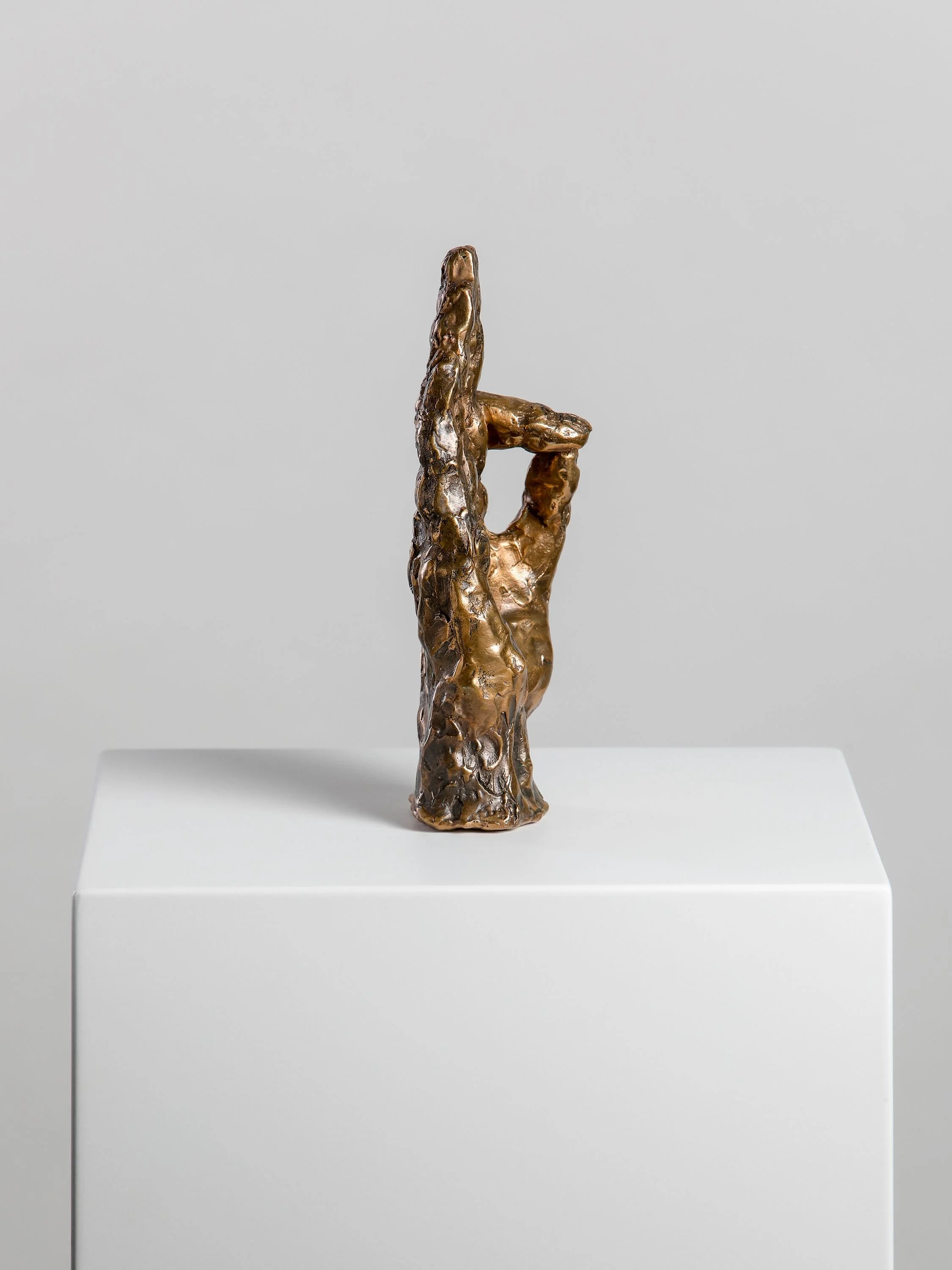Bronze sculpture of a hand with index finger pointing upward, mounted on a white pedestal.