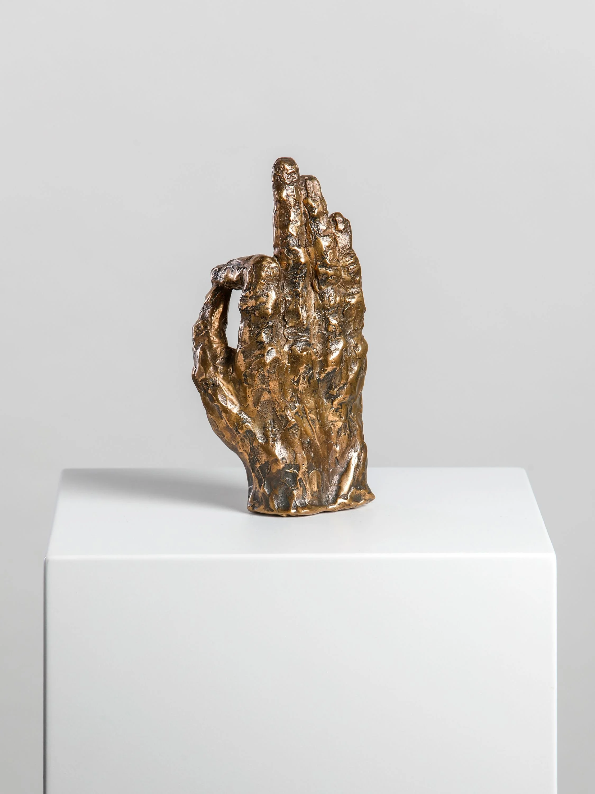Bronze sculpture of a hand with three fingers extended, mounted on a white pedestal.