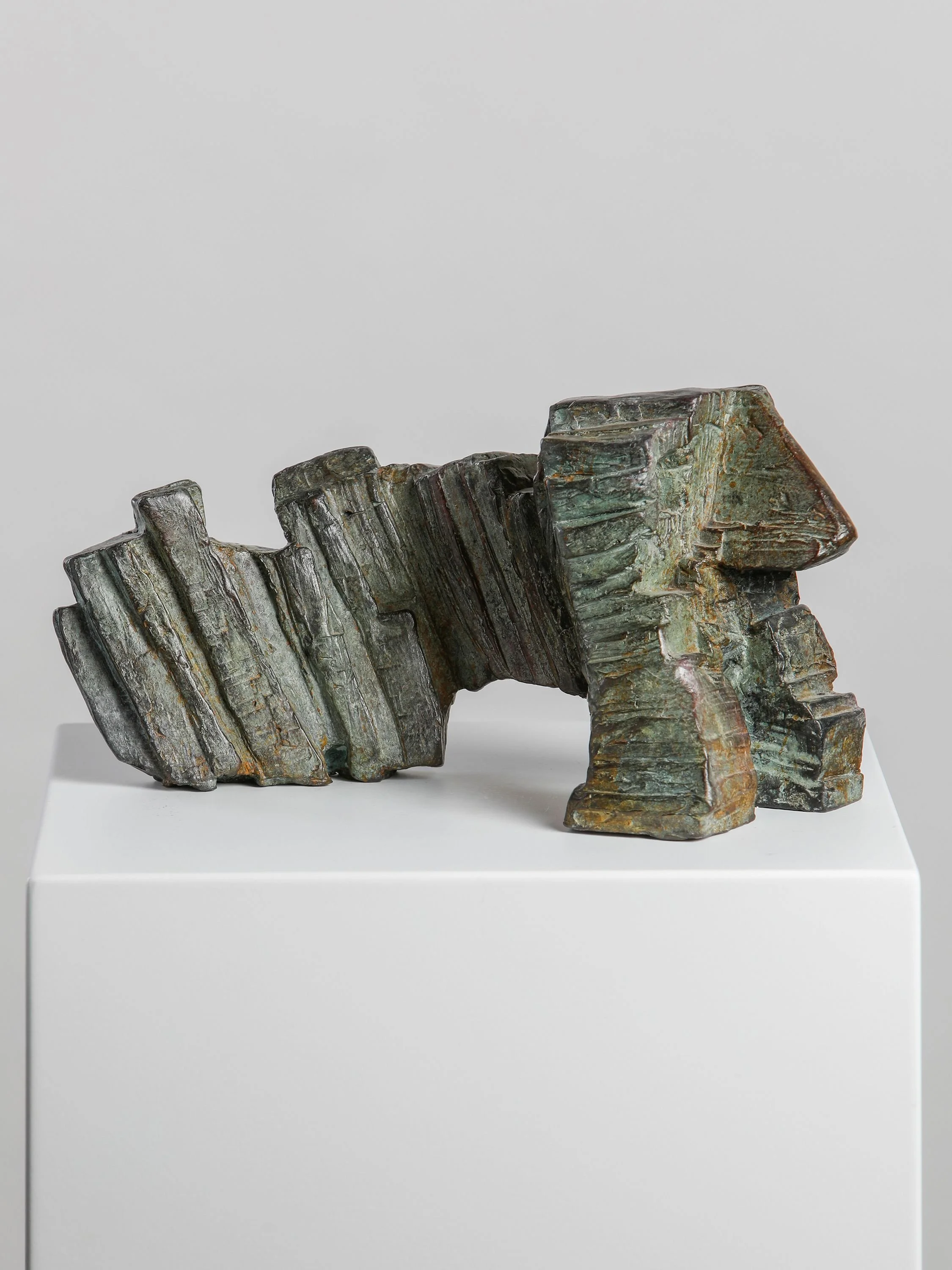 Abstract bronze sculpture with geometric shapes and textured surfaces displayed on a white pedestal.