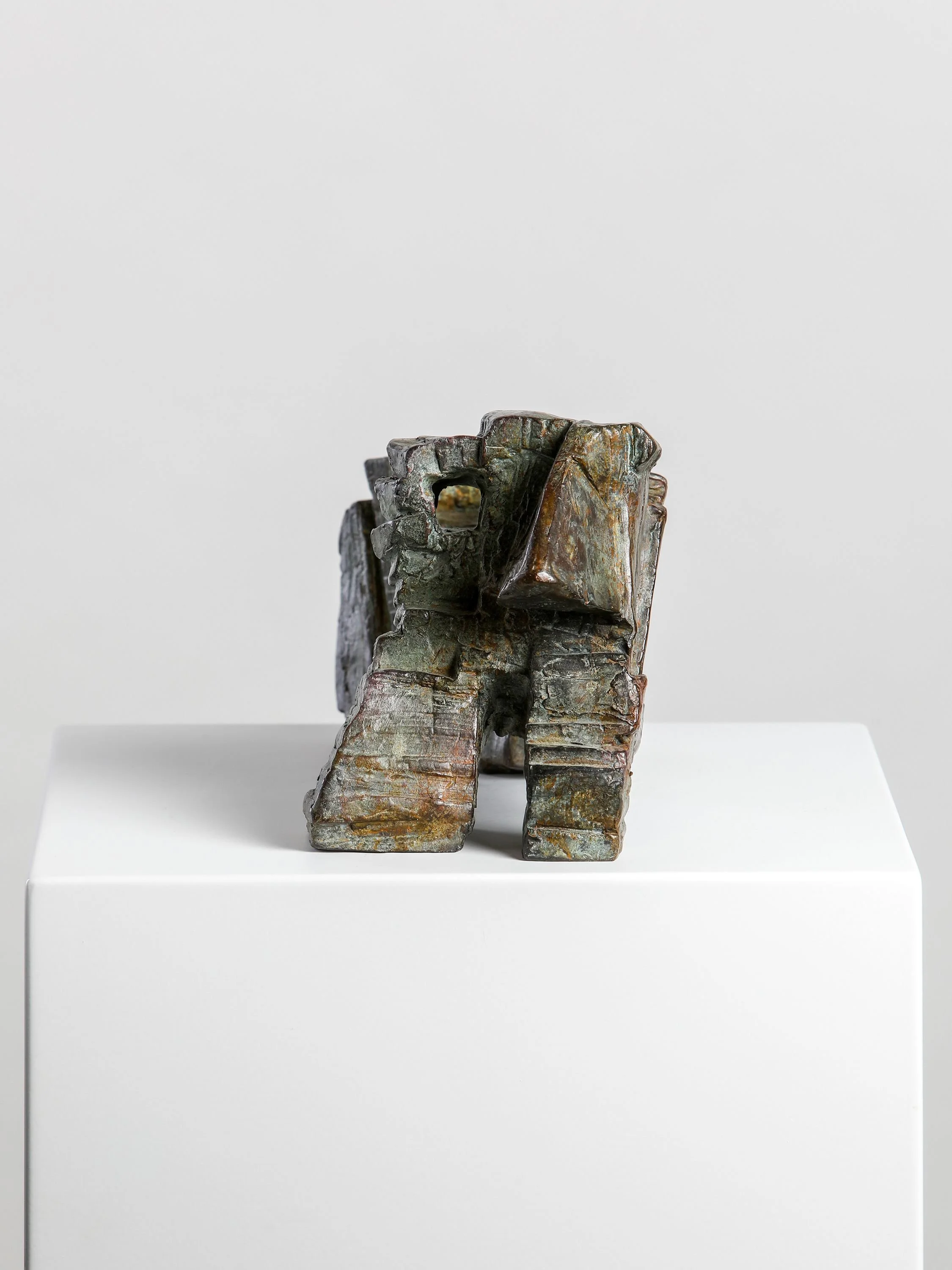 Bronze sculpture of an abstract face with prominent features, displayed on a white pedestal against a gray background.