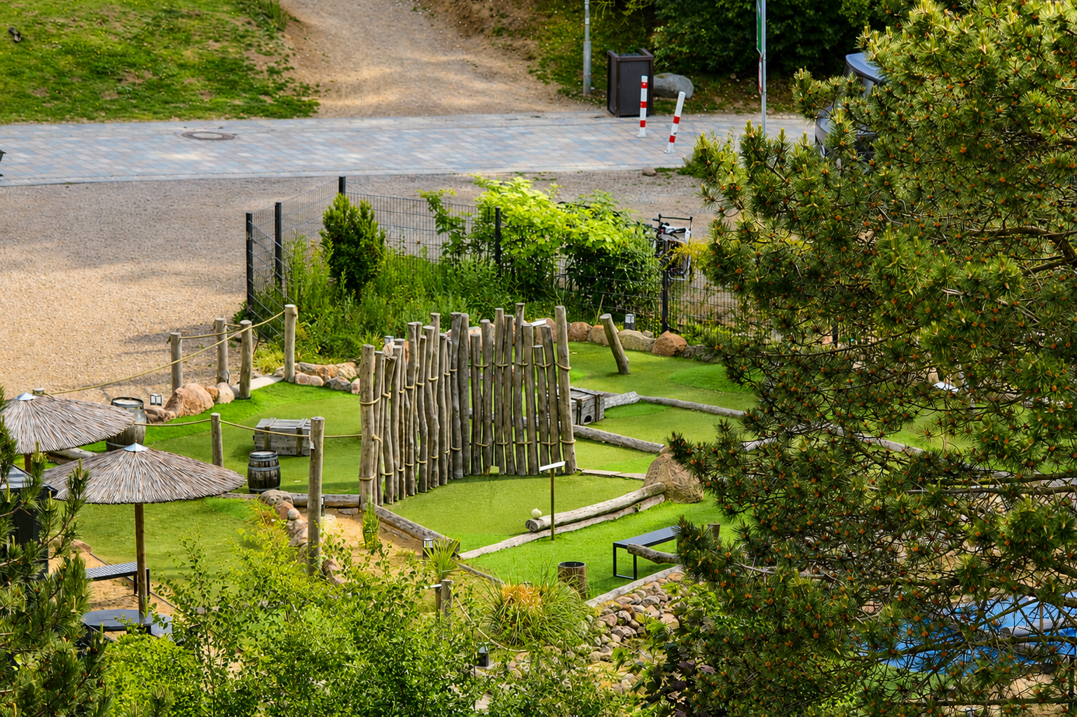 Ein kleiner begrünter Spielplatz mit Holzzäunen, Rasenflächen, Sonnen-Markisen, Baum und beleuchteten Wegen