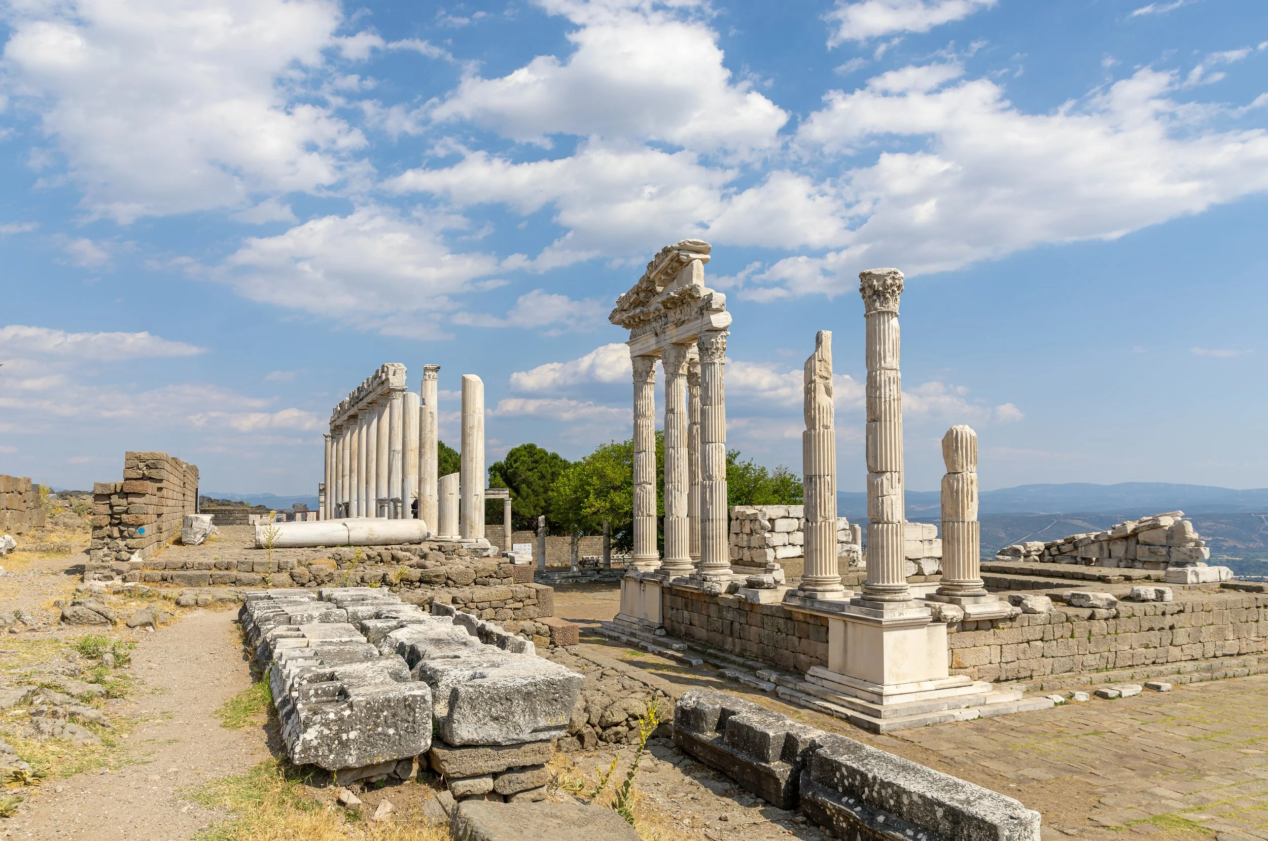 Ancient Greek ruins with broken columns and stone structures under a bright sky with scattered clouds.