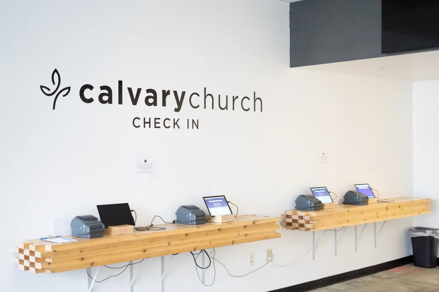 Check-in stations at Calvary Church with wooden counters and electronic devices, wall signage reading 'Calvary Church Check-In'.