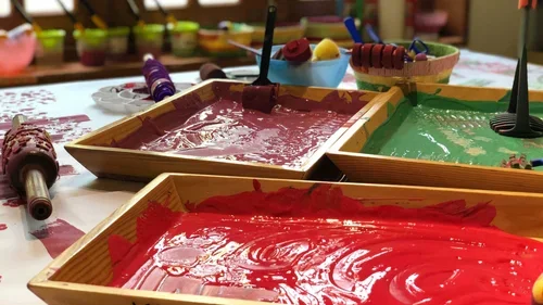 Tables with colorful melted wax or paint, brushes, and craft tools for arts and crafts activities.