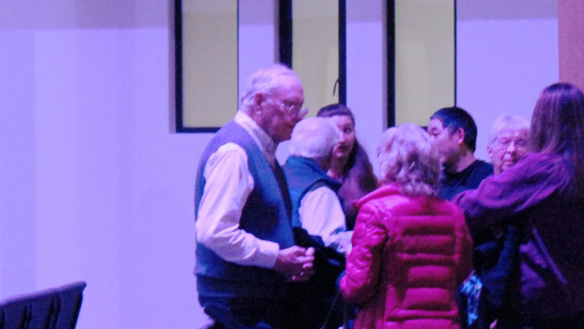 A group of people gathered indoors, engaging in conversation, with purple lighting creating a vibrant atmosphere.