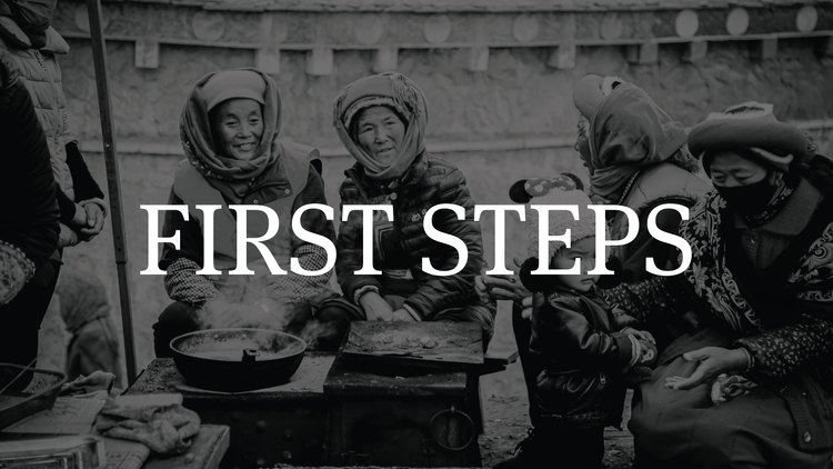 Smiling women and children in headscarves gathered around a cooking stove outdoors, with the words 'First Steps' overlaid.