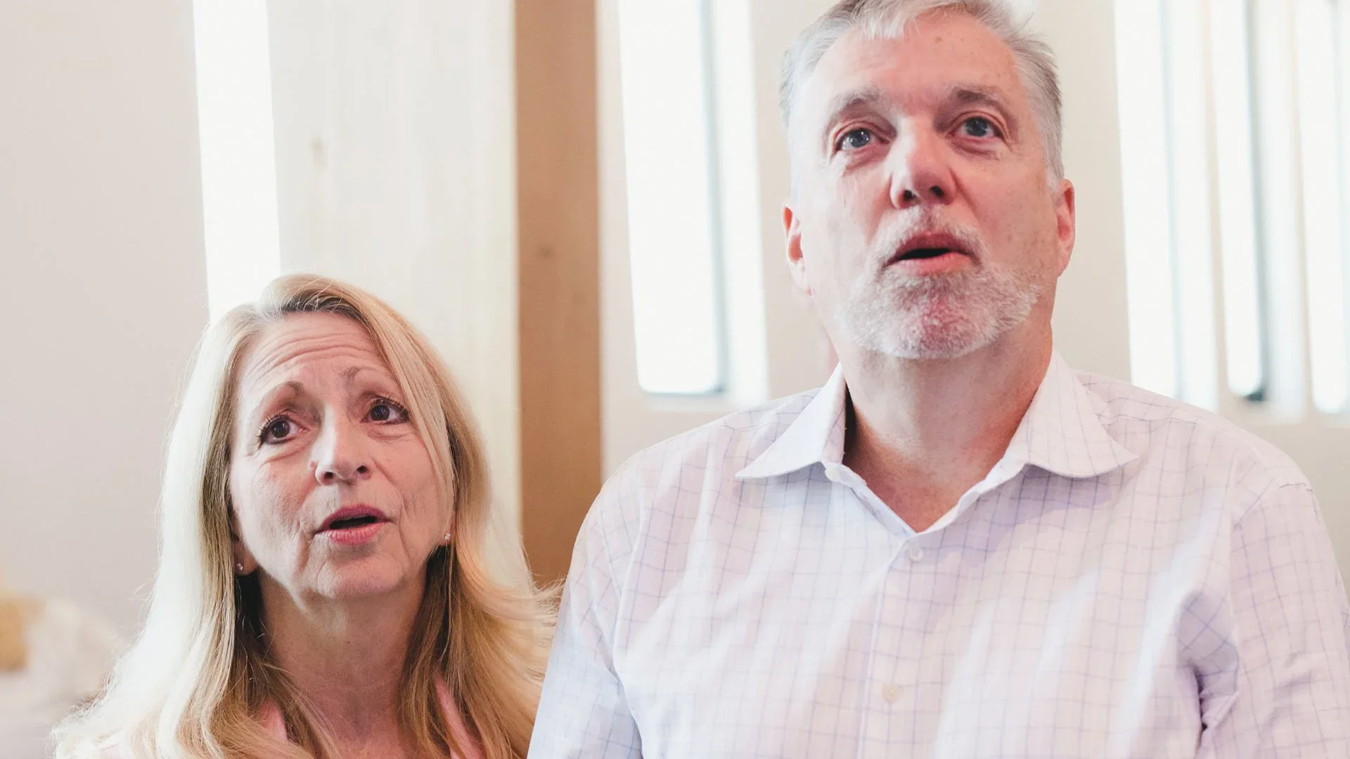 An older woman with long blonde hair and a man with gray hair and beard in a well-lit room.