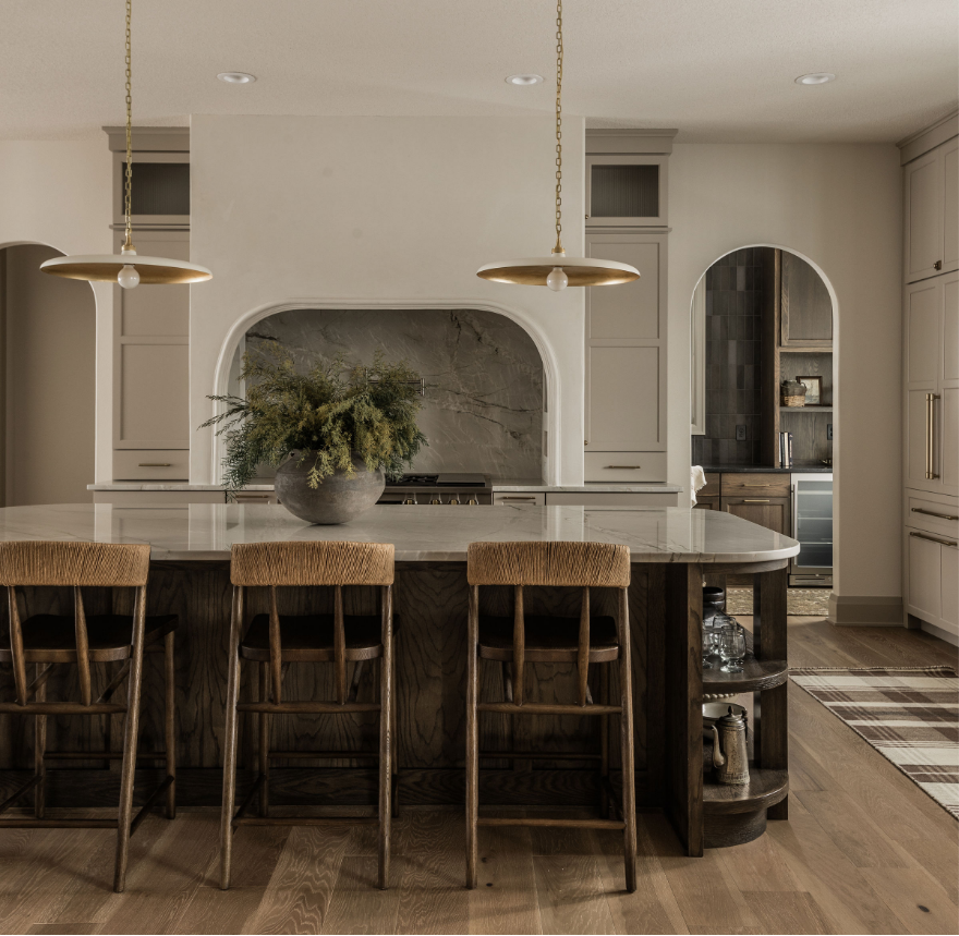 Modern kitchen with an island, four wooden barstools, a large gray vase with greenery, pendant lights, and built-in cabinets.