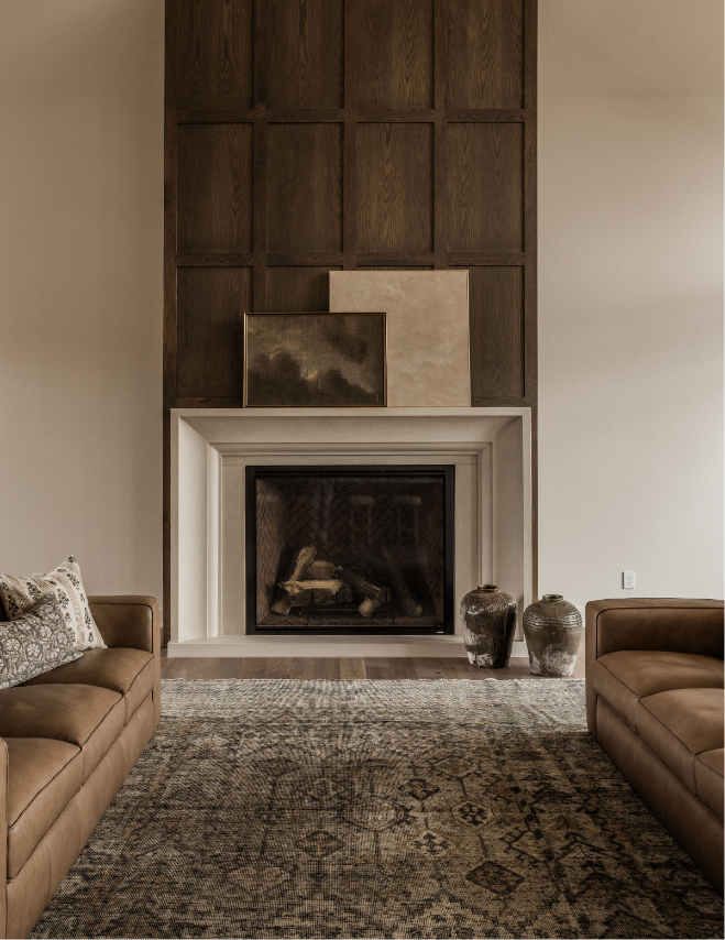 Living room with a white fireplace, two brown sofas, a patterned rug, and decorative vases, with artwork above the fireplace.