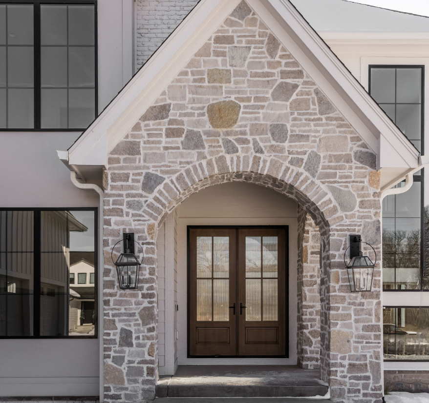 Front entrance of a house with stone archway, double wooden doors, and wall-mounted lanterns.