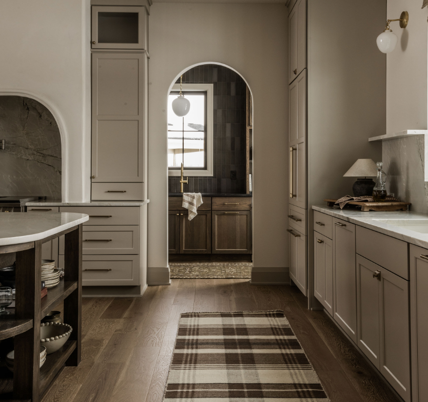 Kitchen with white and wood cabinets, a small window, and a plaid rug on wooden floor.