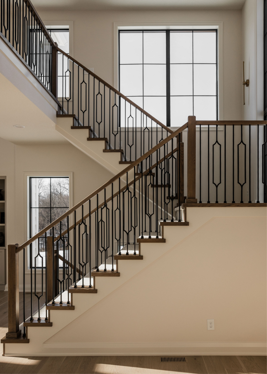 Interior view of a staircase with wooden steps and black metal railings, leading to an upper floor with large window with multiple panes.