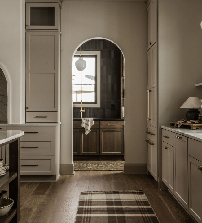 Kitchen view through an arched doorway showing a window with natural light, dark wood cabinets, a hanging light fixture, and a towel at the sink
