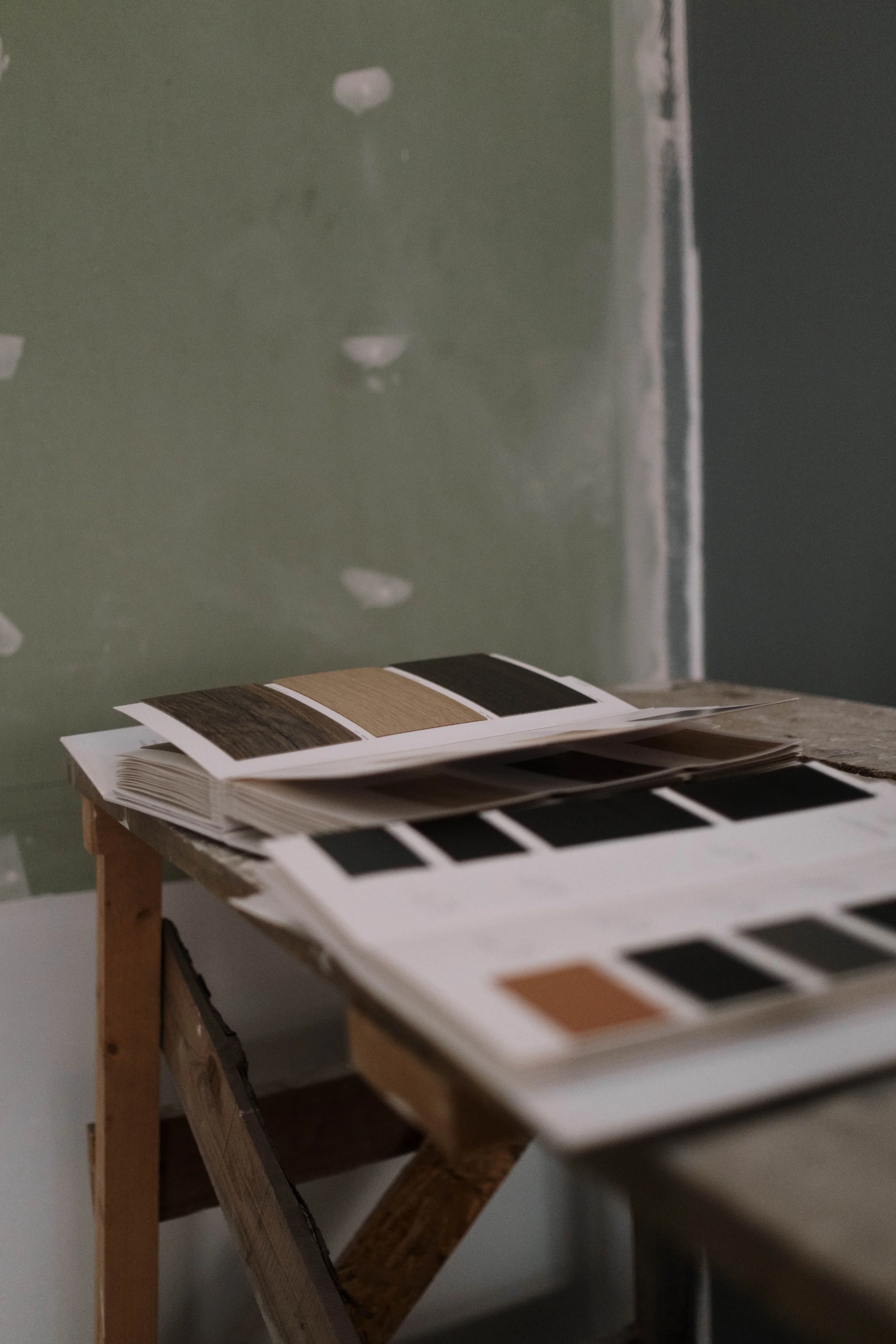 Open paint color sample book with various samples on a wooden table in a room with green walls.