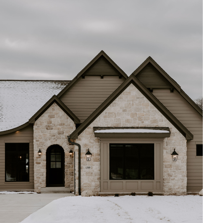 Front of a house with stone and siding exterior, three peaked roofs, and snow on the ground.