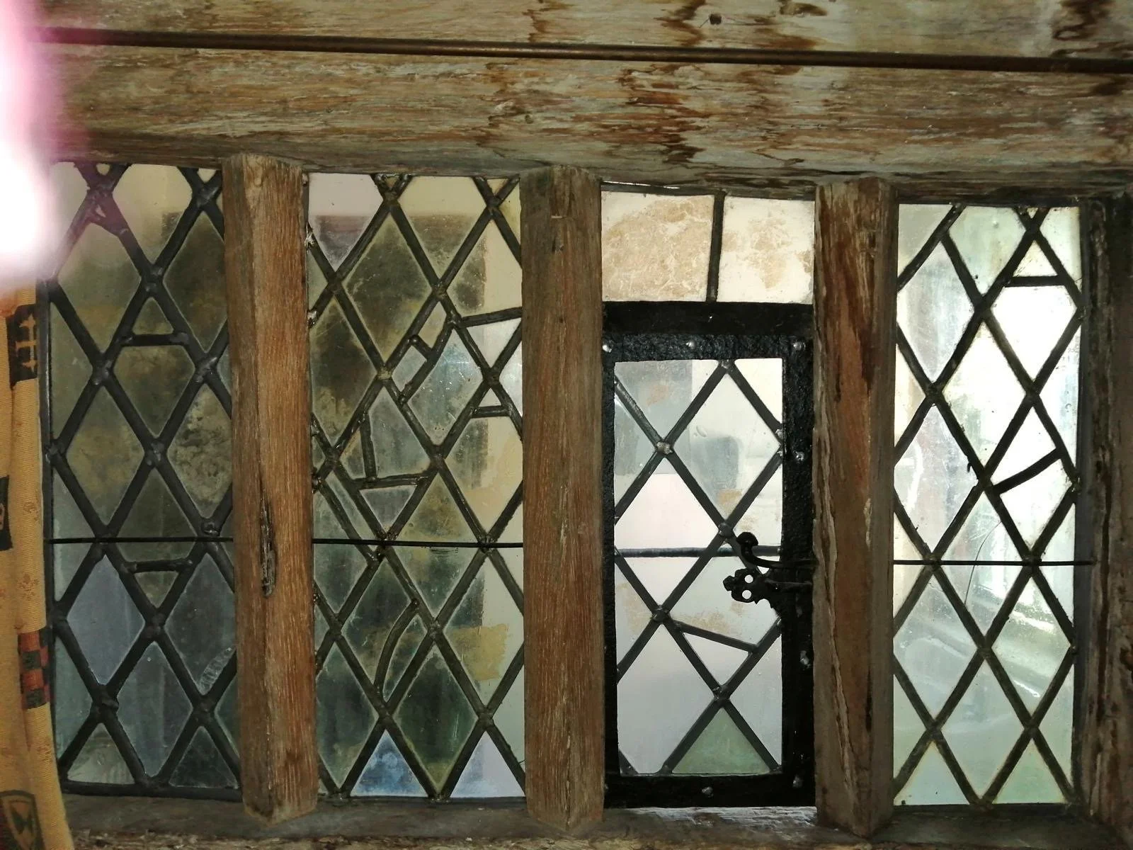 Close-up view of a small window with metal lattice and a wooden frame, part of an old building or structure.