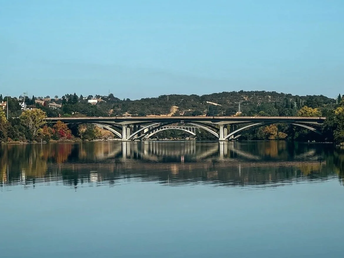 A bridge over a calm river with reflections of trees and hills in the water.