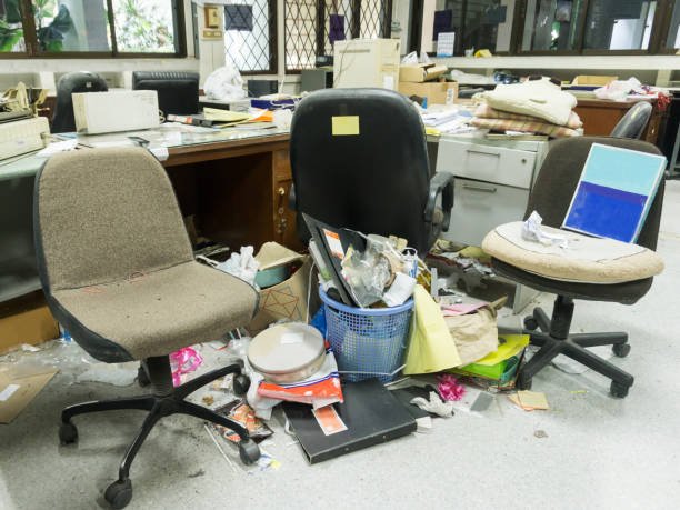 Three messy office chairs surrounded by trash, papers, and clutter on the floor and desks in an office.