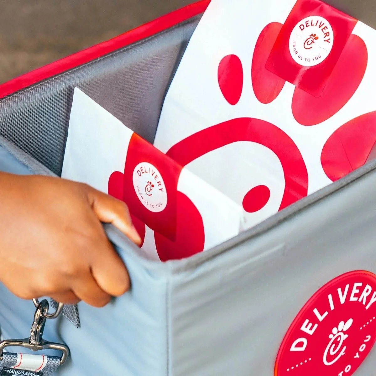 Close-up of a hand opening a delivery bag with red and white branding, containing white paper with red paw print designs and delivery stickers.