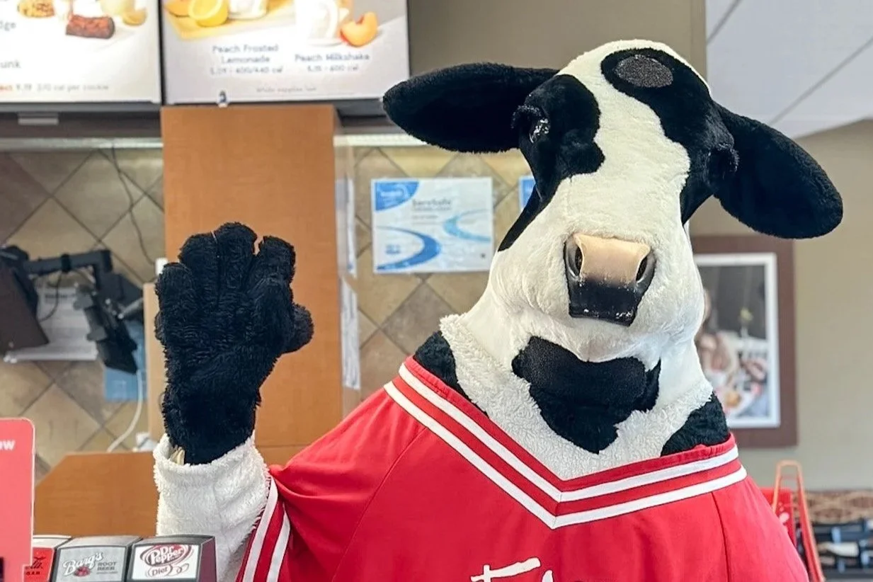 The Chick-fil-A Cow wearing a red sports jersey, standing inside a Chick-fil-A