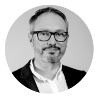 Black-and-white portrait of a man with glasses, short hair, and a goatee, wearing a suit jacket and collared shirt.
