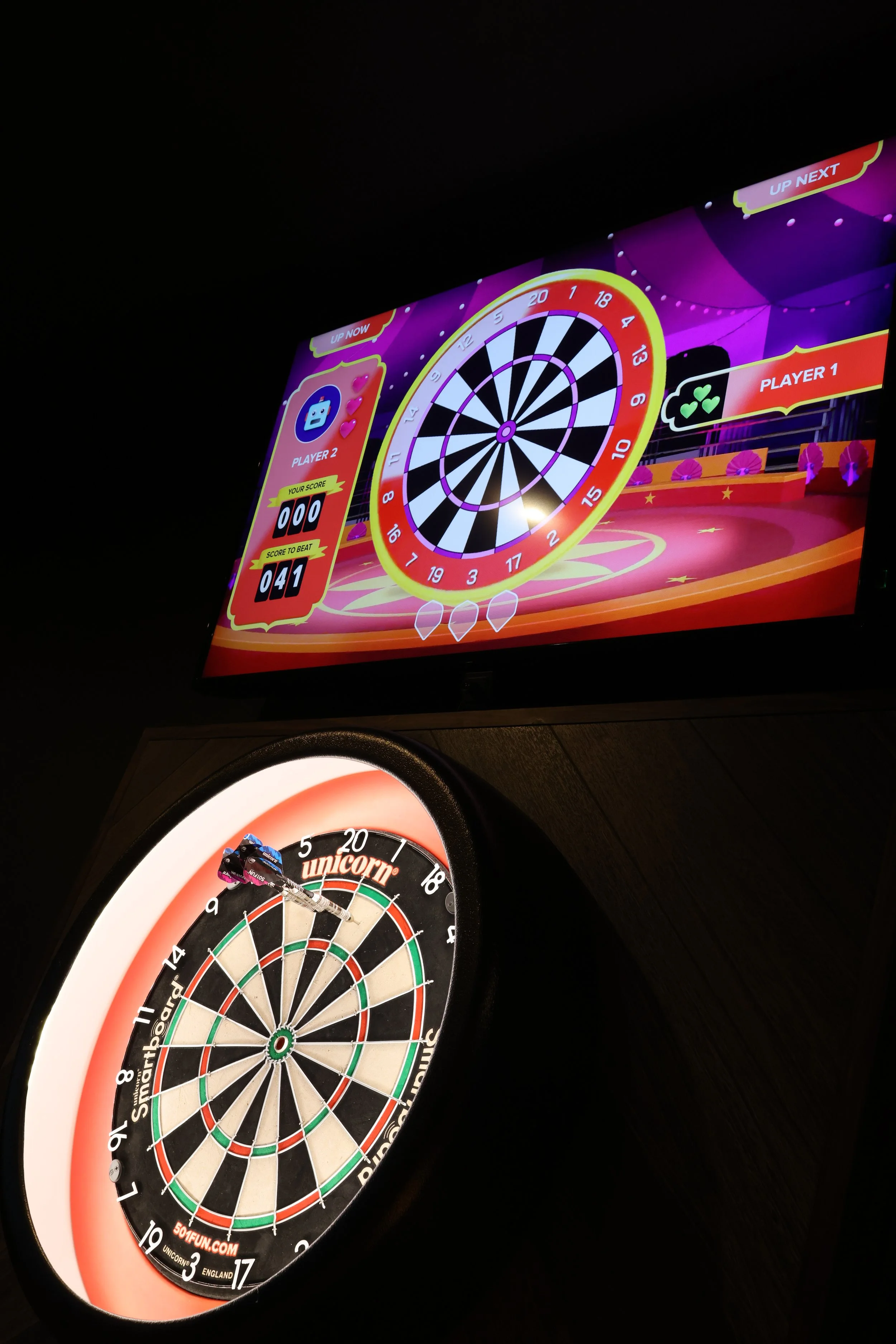 Two electronic dartboards in a dark room, one showing a game in progress and the other with a colorful circular target.