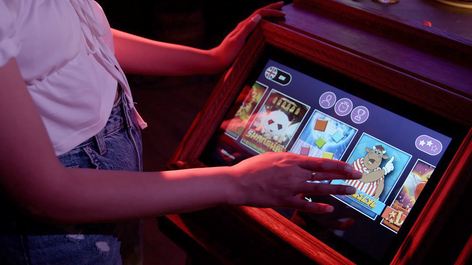 Person using a touchscreen device to browse digital game store, selecting game with cartoon character on screen, in a setting with dim lighting.