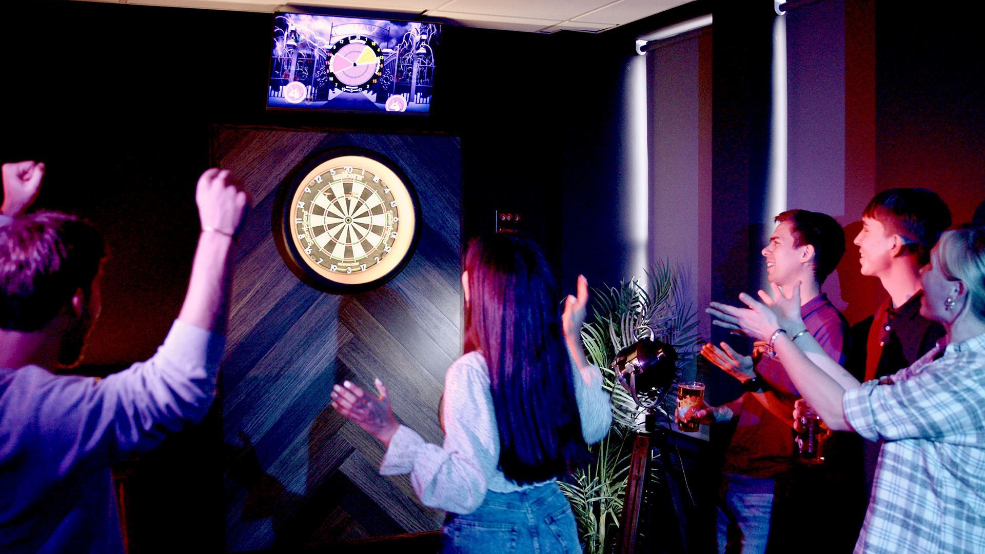 Group of people playing and celebrating while participating in a dart game in a dimly lit indoor setting.